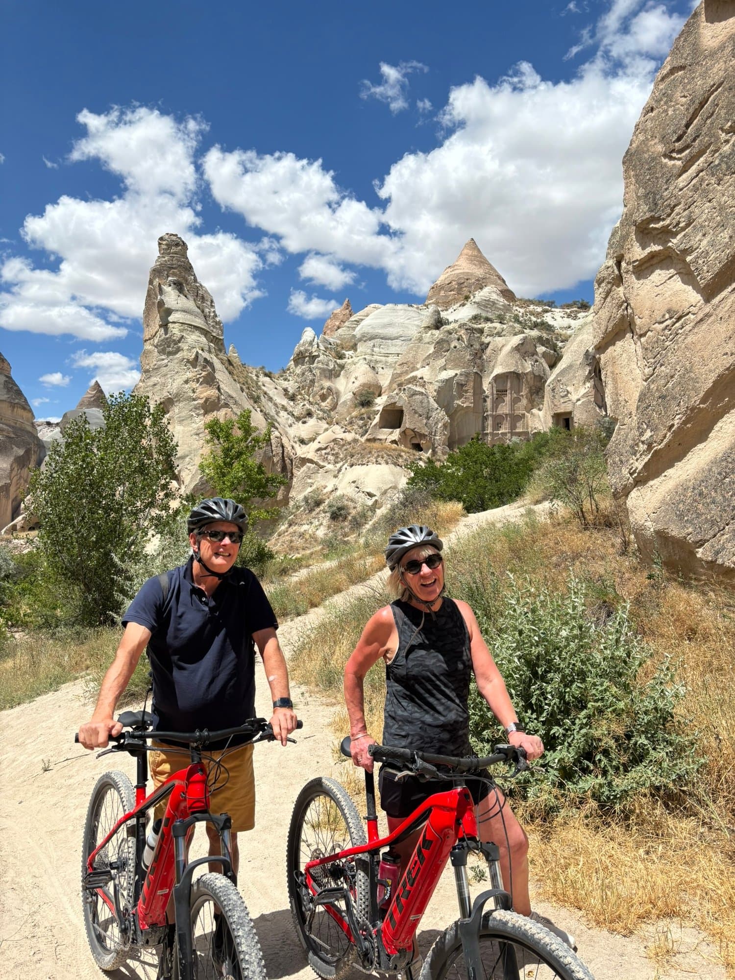 Two smiling riders with their red Trek e-bikes among the fairy chimneys of Cappadocia