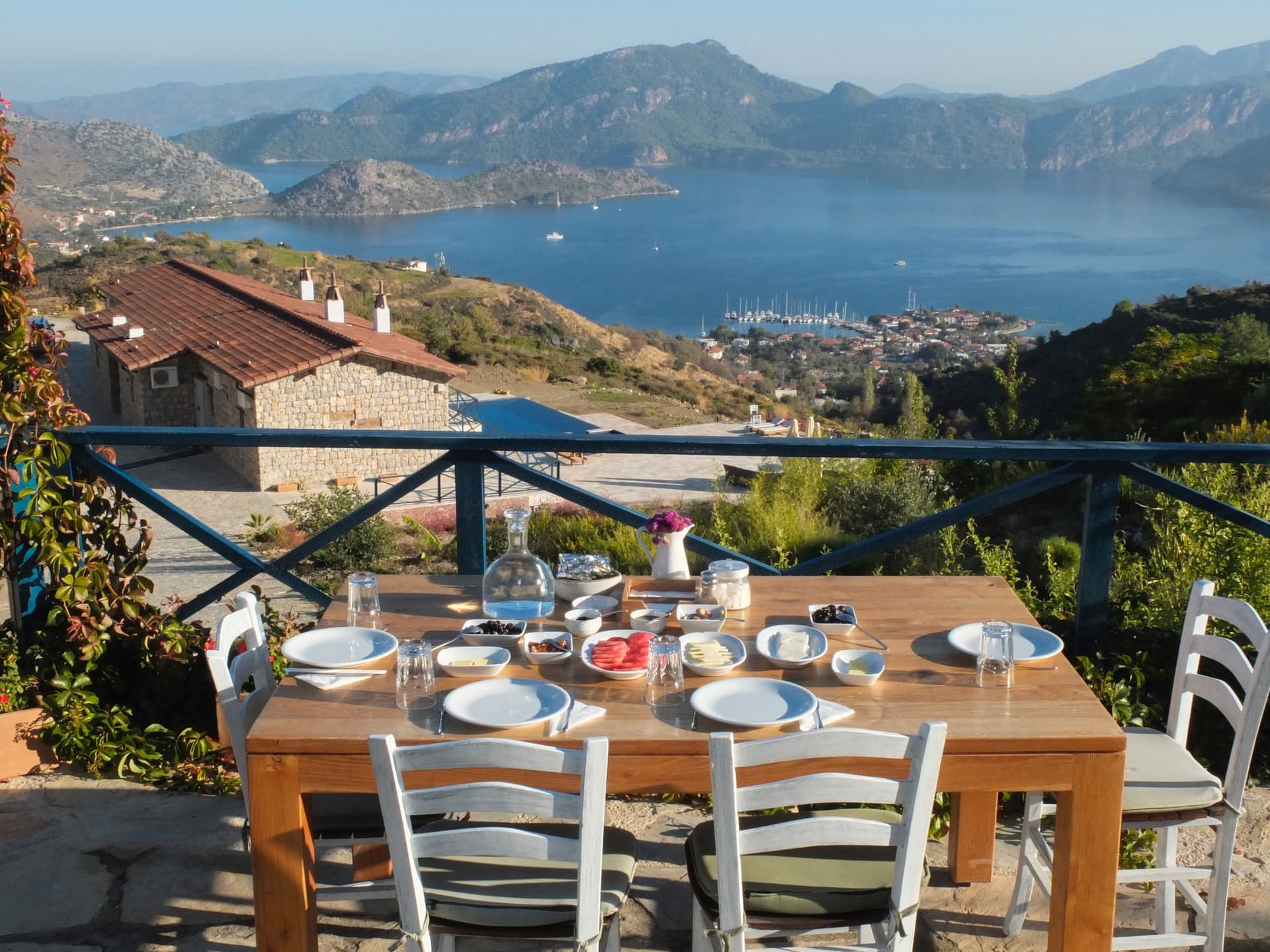 Breakfast table set on a terrace overlooking an Aegean bay and hillside village