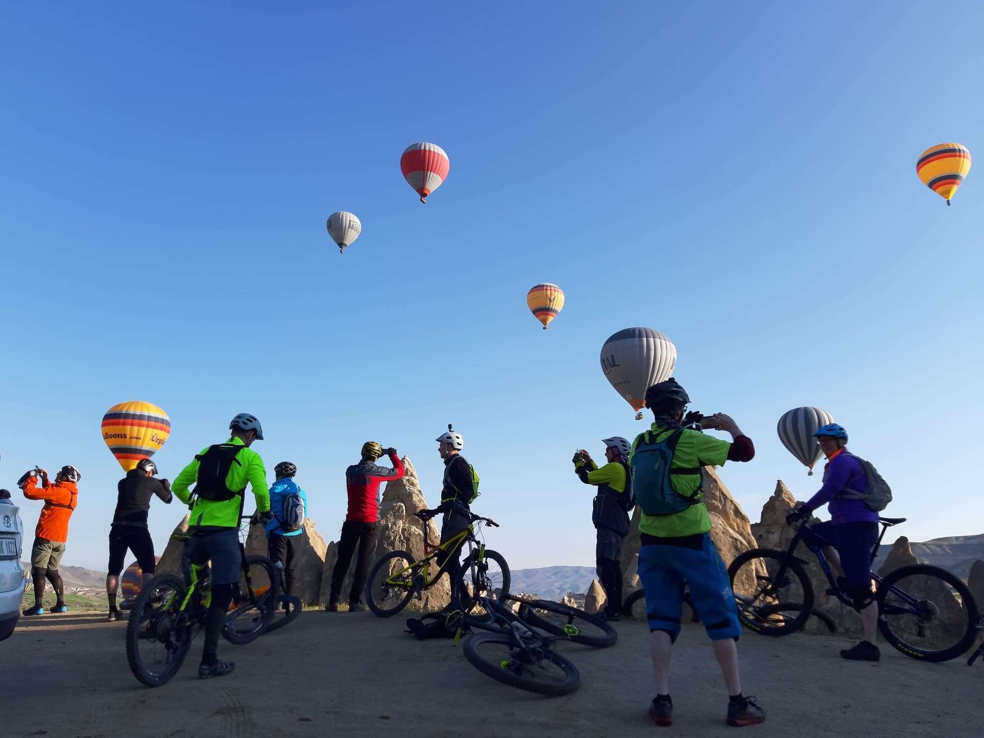 Mountain bikers in Cappadocia, Turkey, watching hot air balloons over the fairy chimneys.