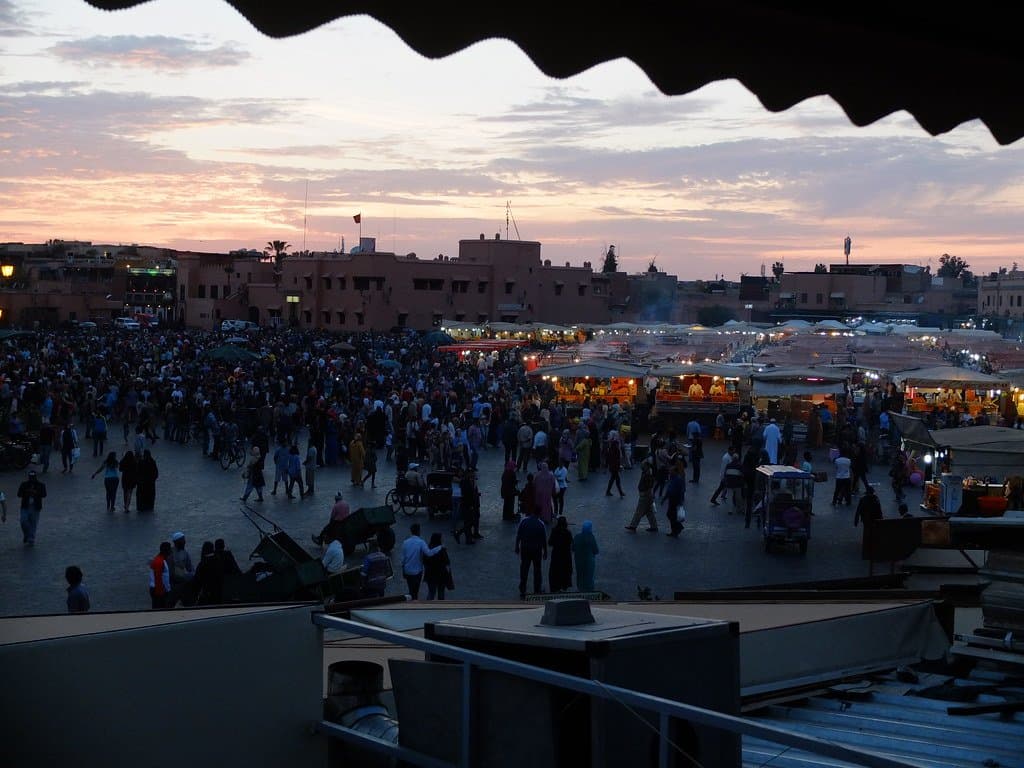 Crowded evening square with food stalls under a colorful sunset sky in Morocco