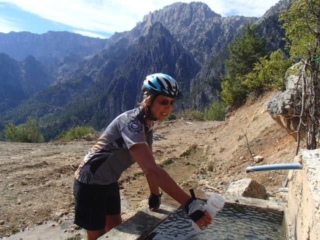 Cyclist filling a water bottle at a stone fountain in the Taurus Mountains
