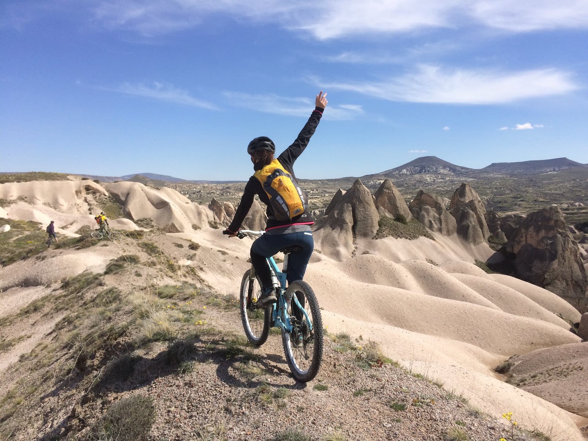 Cyclist raising an arm while riding a ridge lined with fairy chimneys in Cappadocia