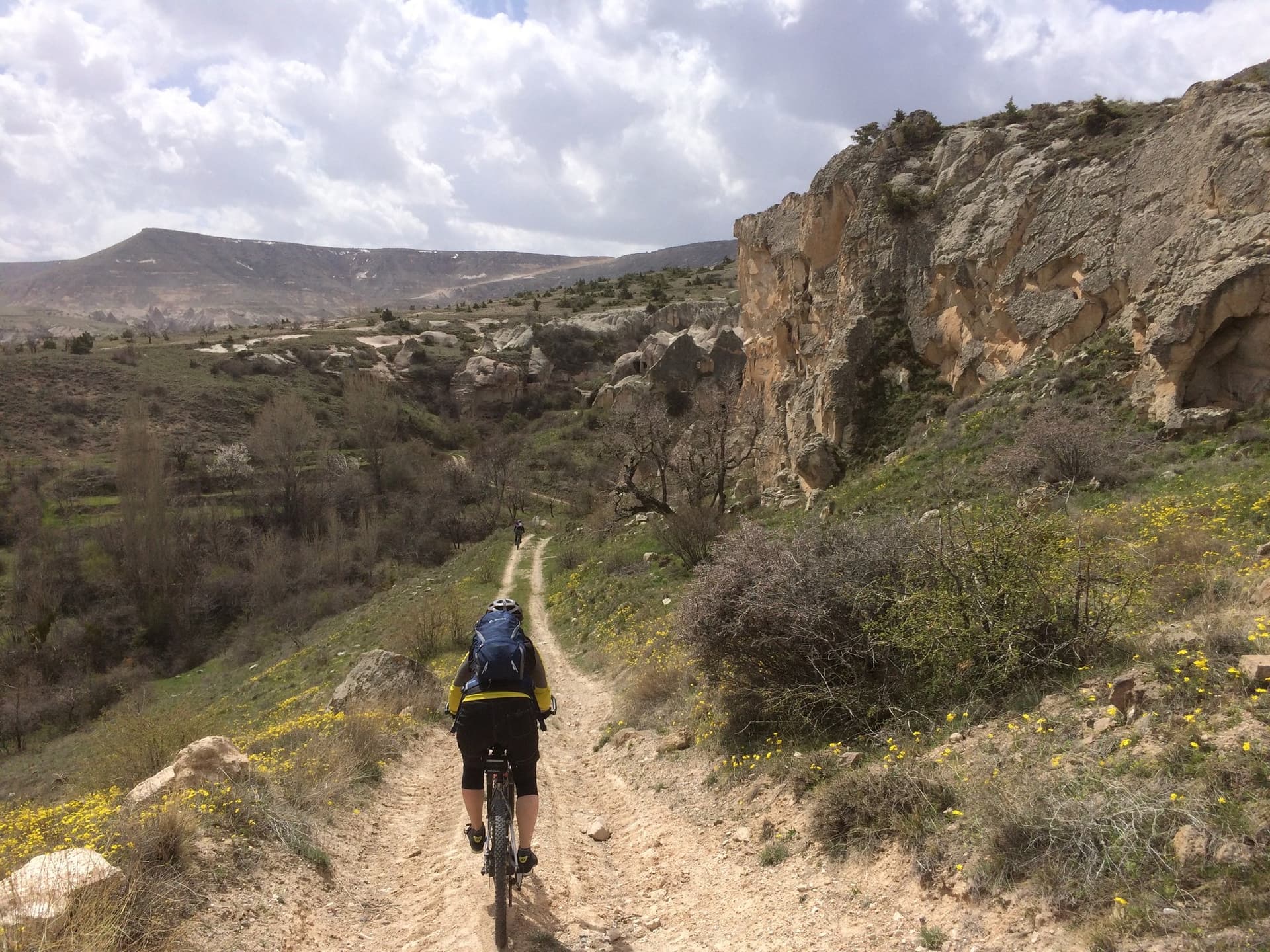 Cyclist riding a dirt trail along a cliff edge dotted with wildflowers in Cappadocia