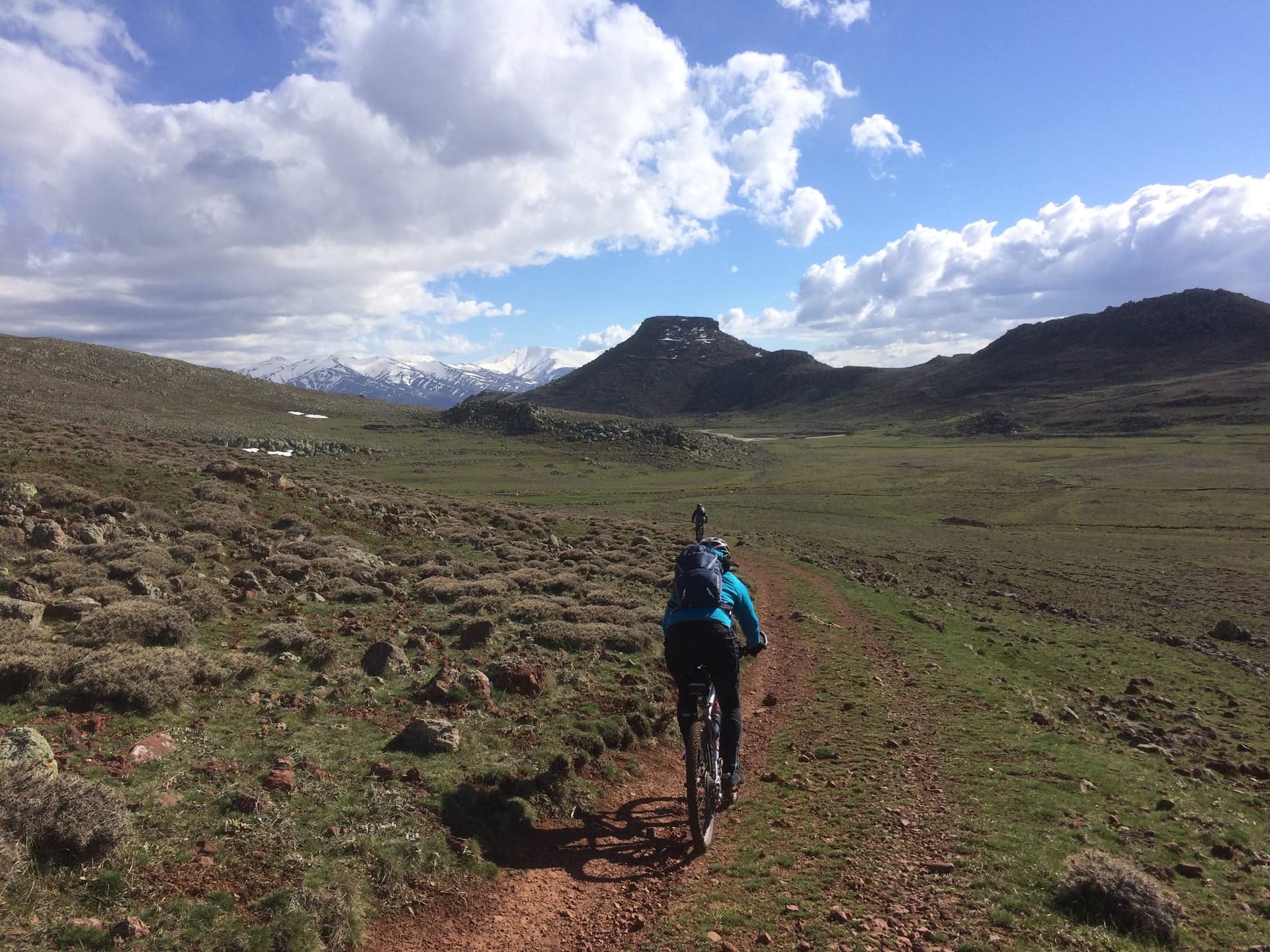 Cyclist riding a dirt trail across open grassland toward a rocky peak
