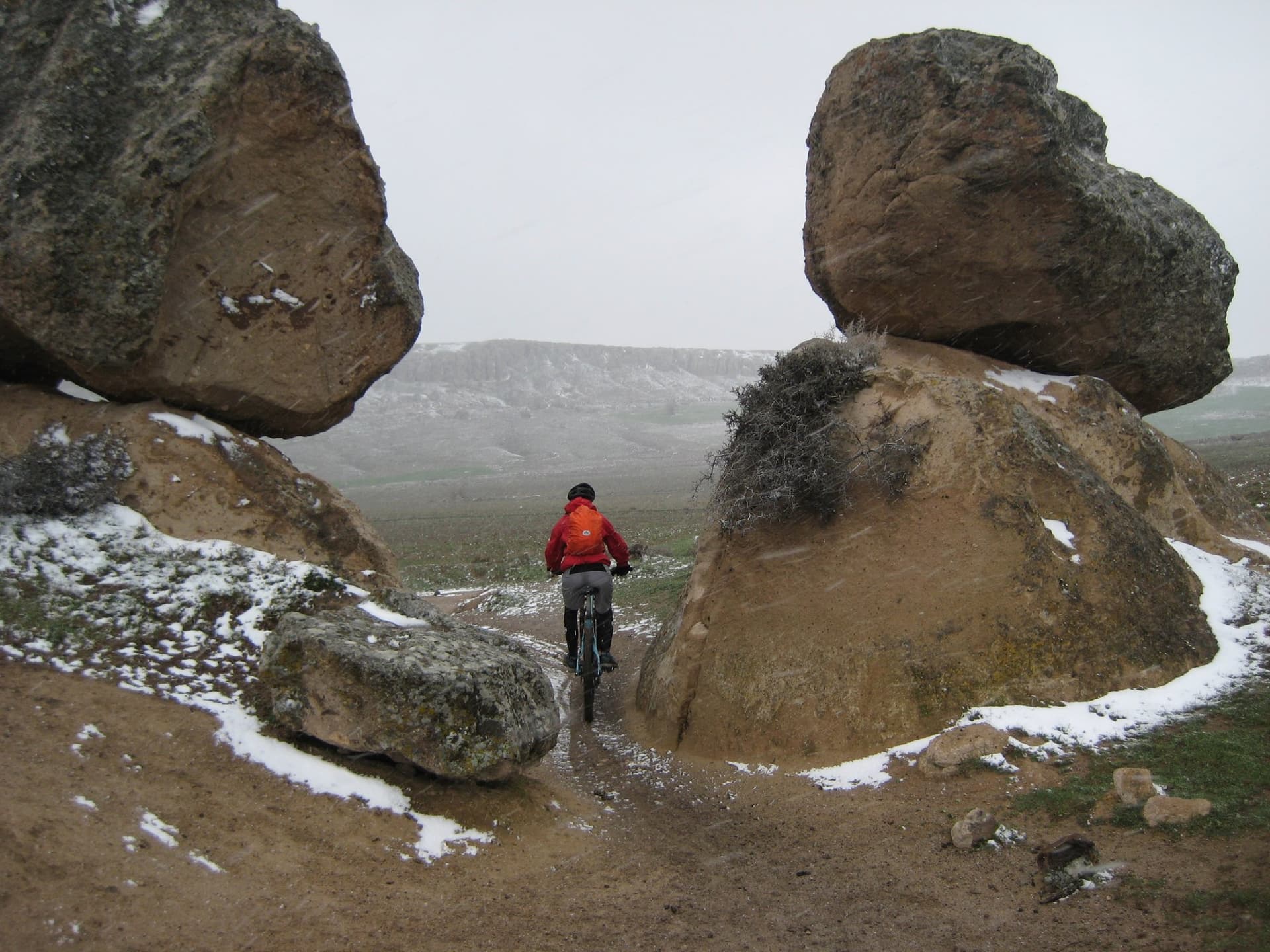 Cyclist riding through a gap between two huge boulders dusted with snow in Cappadocia