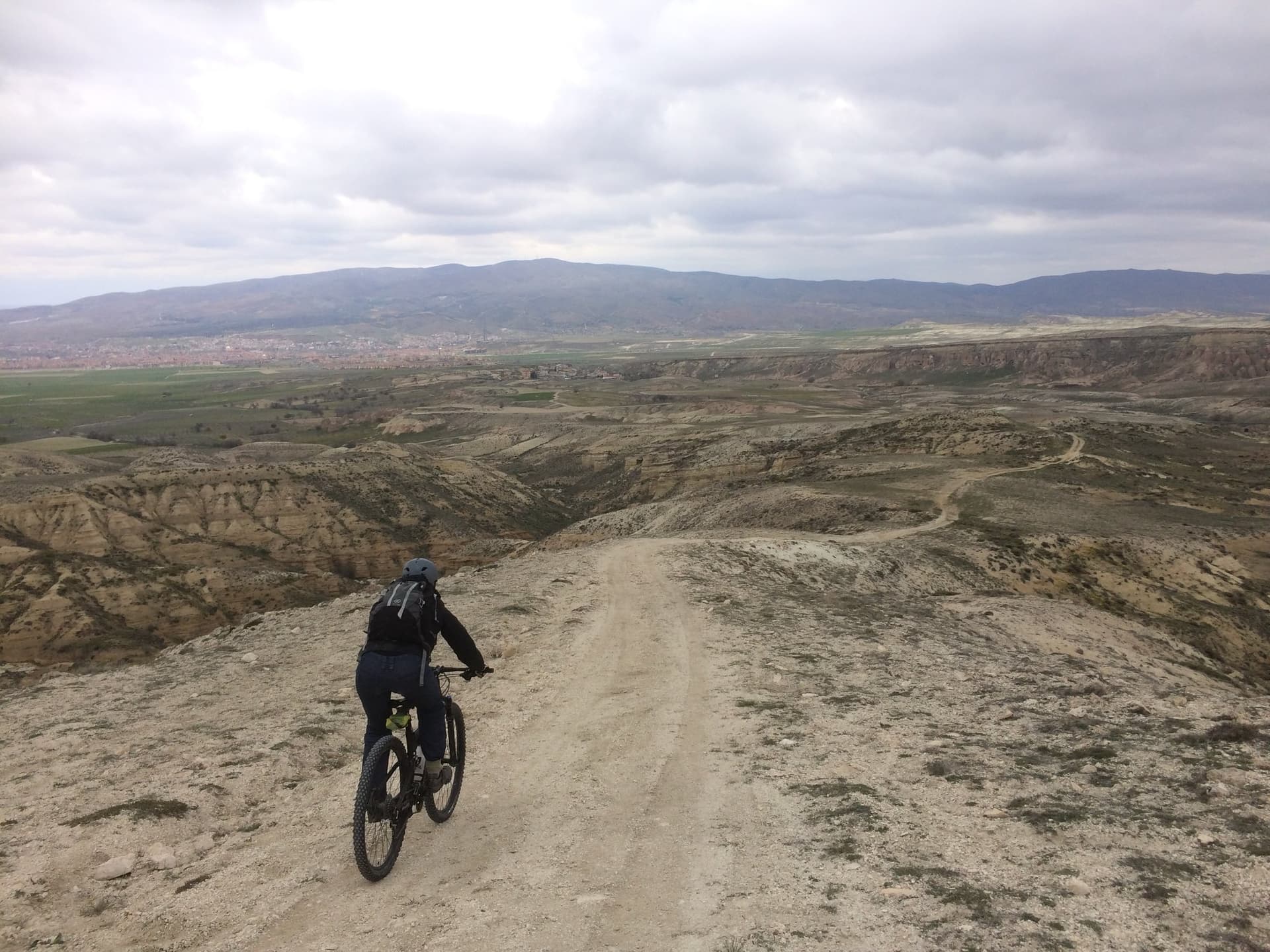 Cyclist riding a gravel road across an open plain toward distant hills