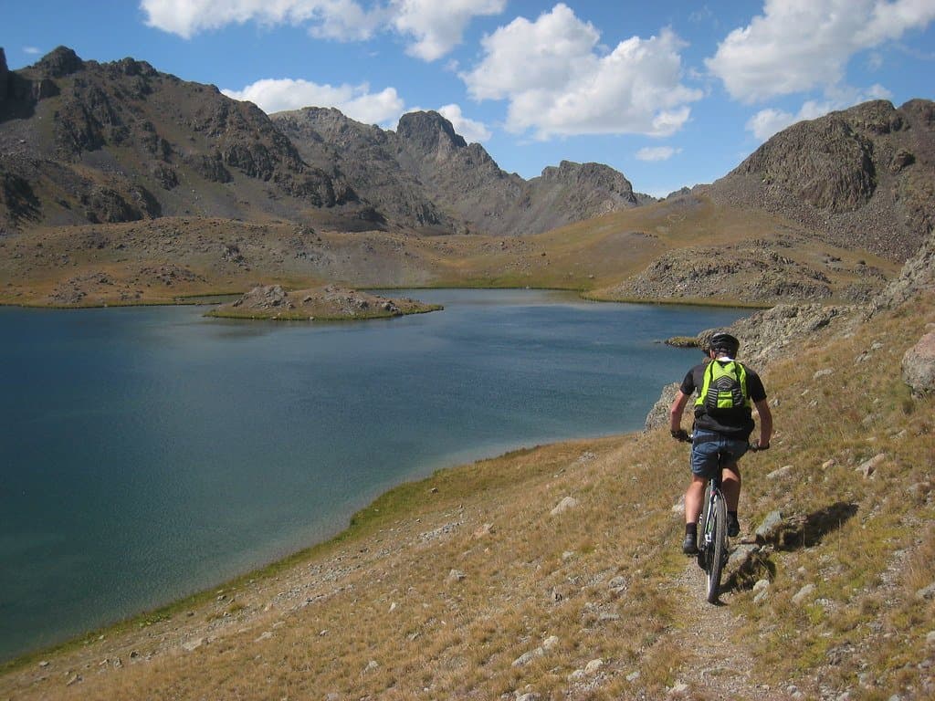 Cyclist riding a gravel trail above a blue lake in the Atlas Mountains, Morocco