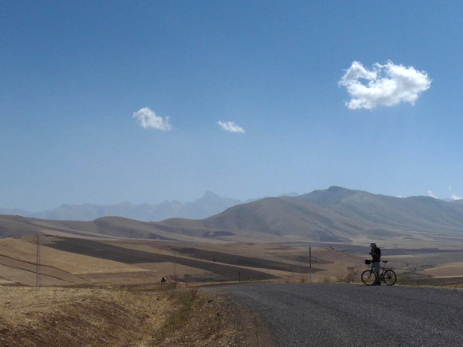 Cyclist riding a paved road through golden steppe hills in Cappadocia