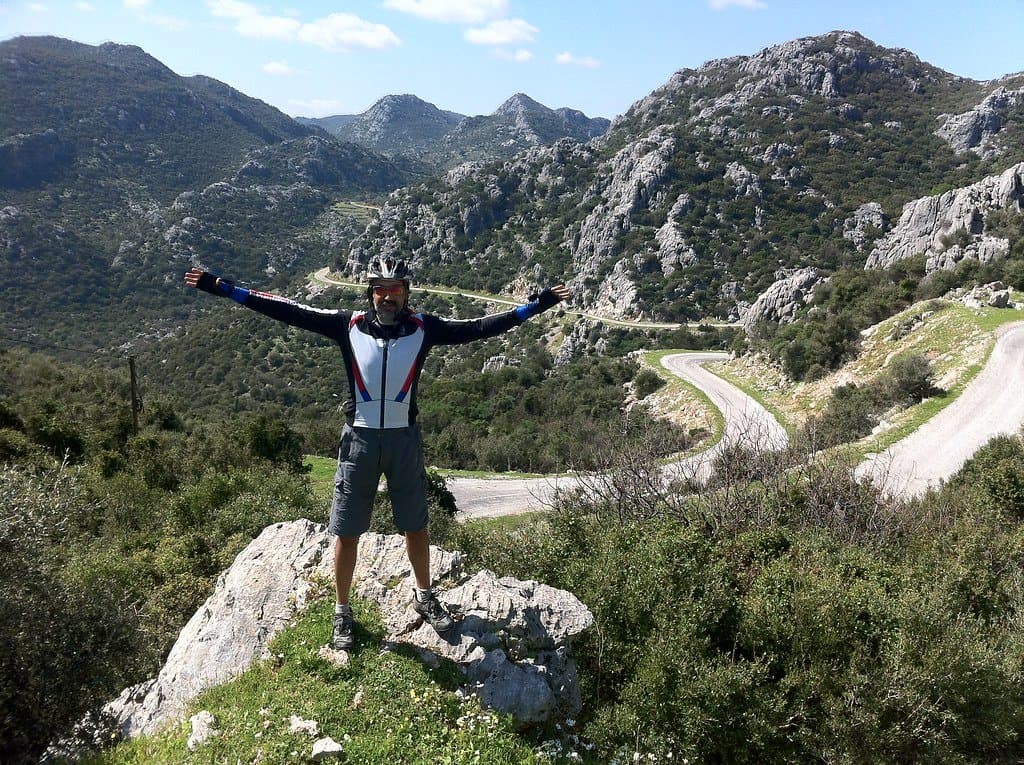 Cyclist standing with arms raised above a winding mountain road