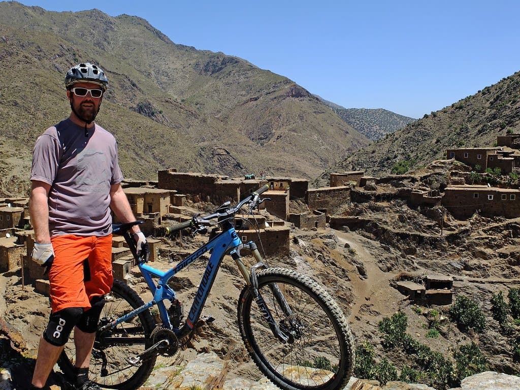 Cyclist standing above a stone Berber village built into a hillside in Morocco