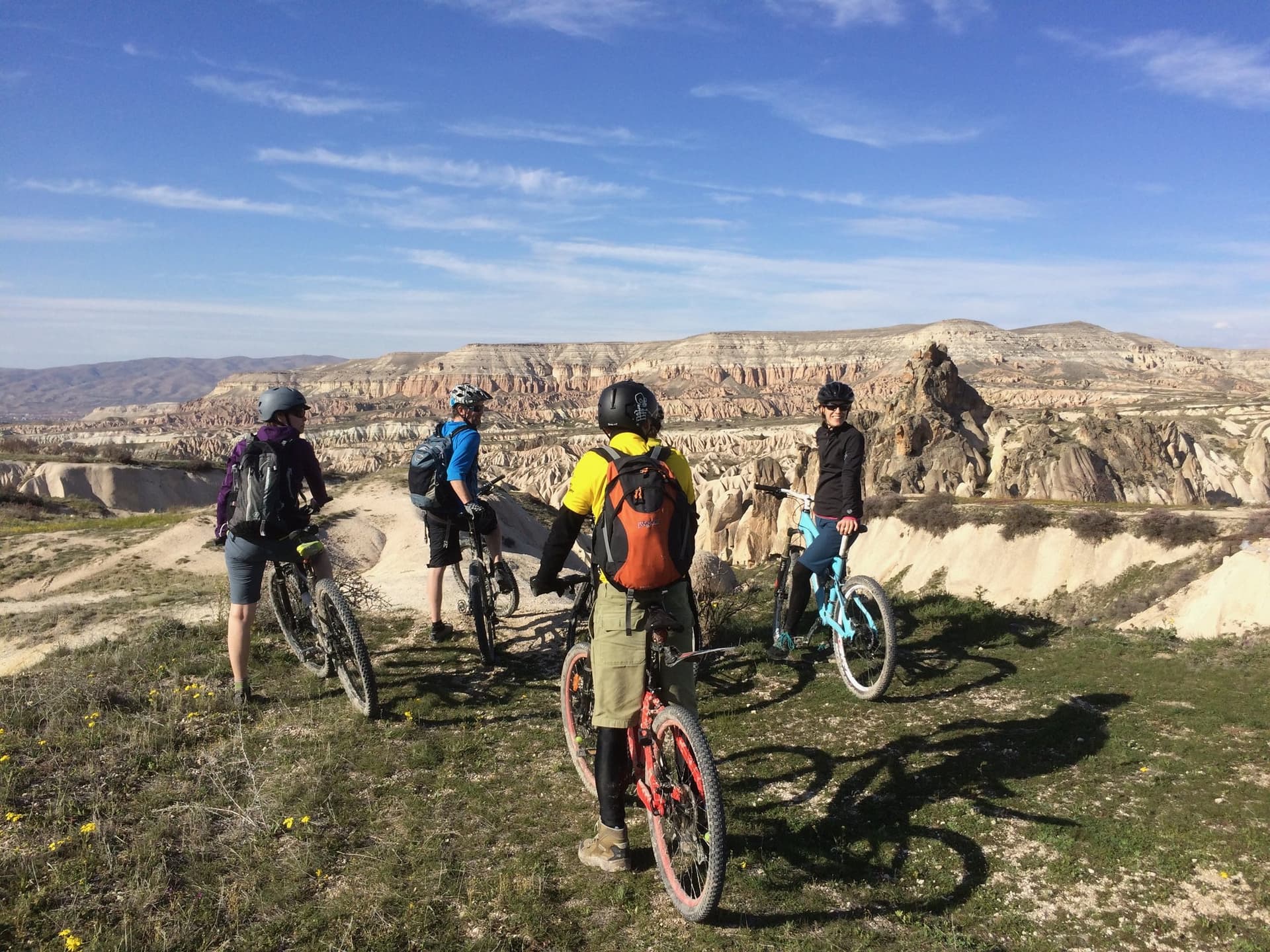 Cyclists with their bikes pausing on a ridge above a rocky Cappadocia valley
