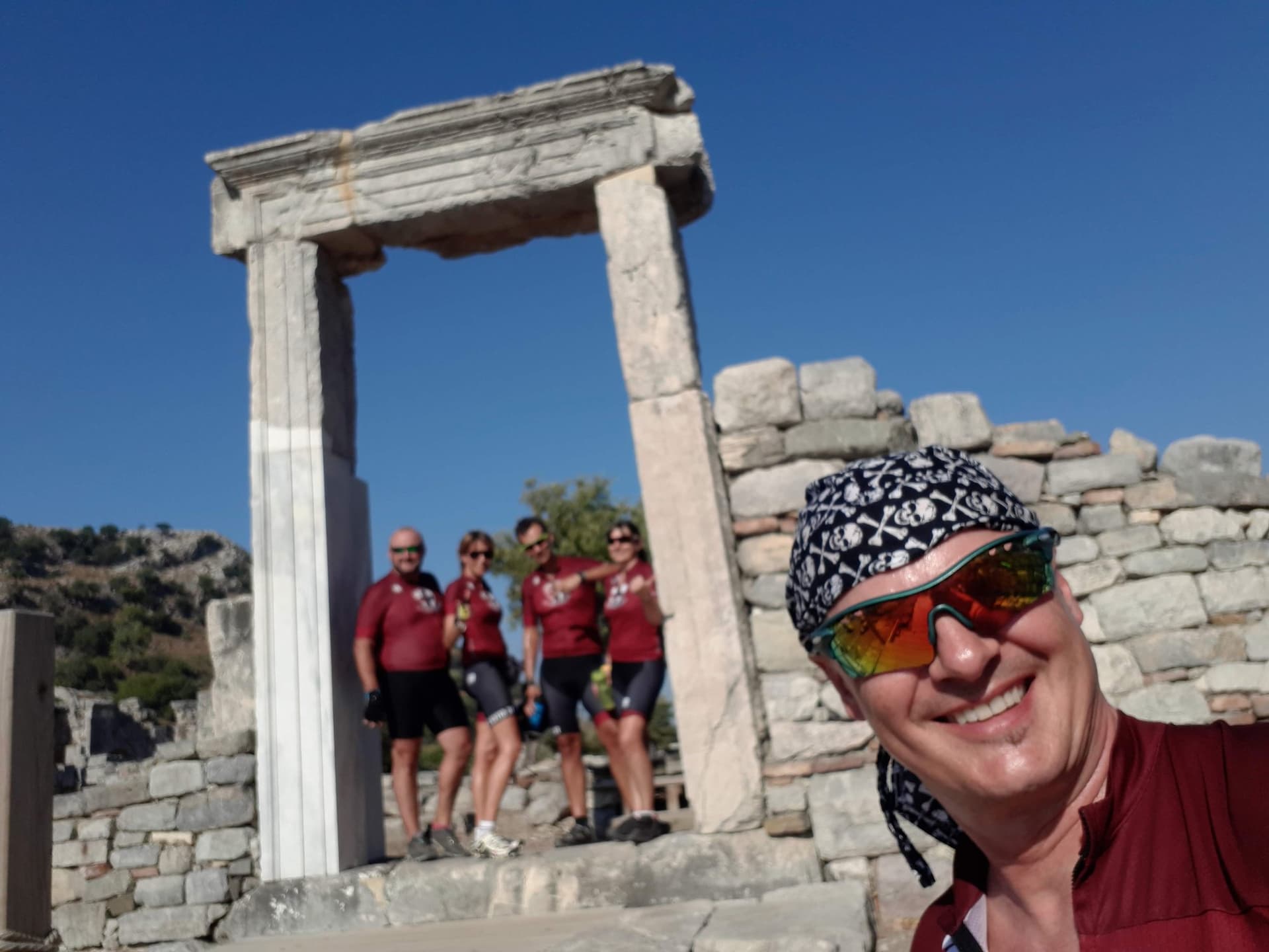 Cyclists posing at an ancient stone gateway on the Aegean coast