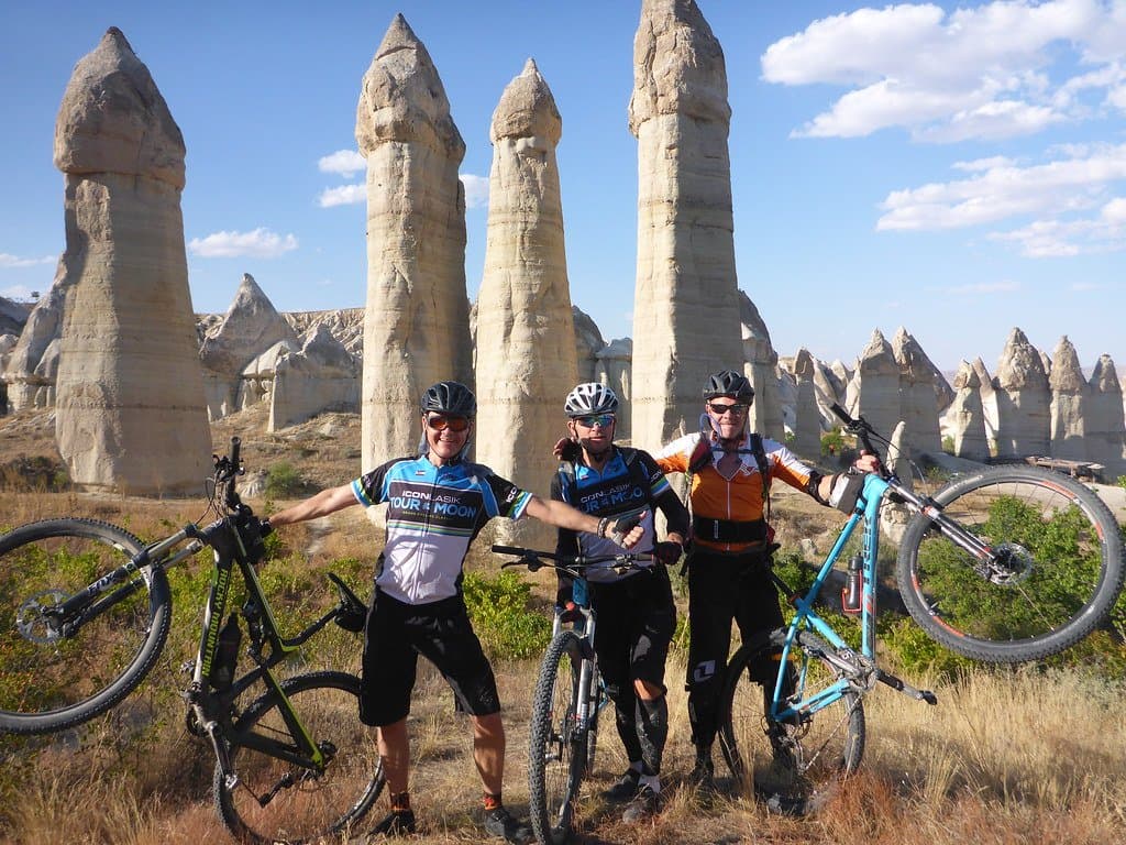 Three cyclists posing with their bikes among tall fairy chimney rock formations