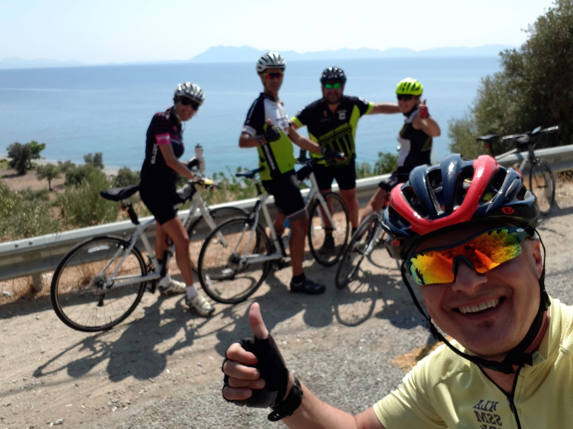 Cyclists posing with their bikes on a roadside above the Aegean coast