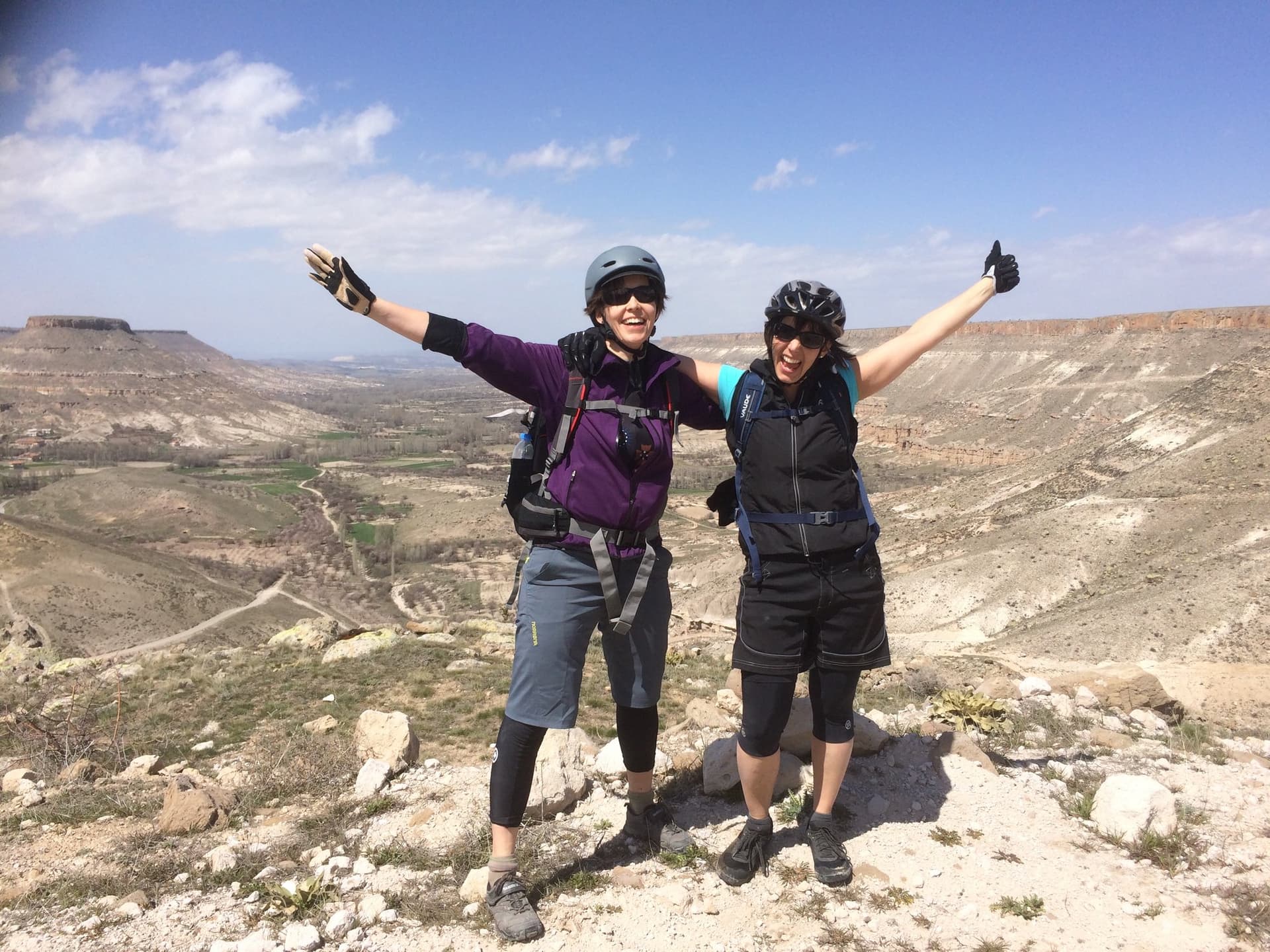 Cyclists raising their arms on a rocky ridge above a Cappadocia canyon
