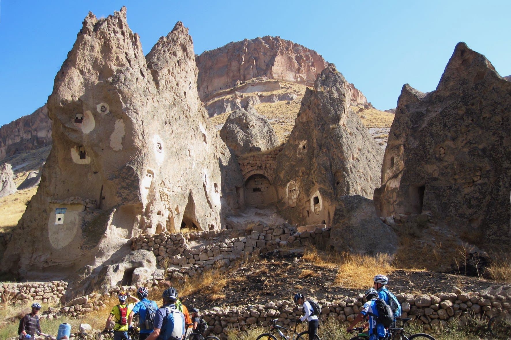 Cyclists riding beneath tall rock spires and cave dwellings in Cappadocia