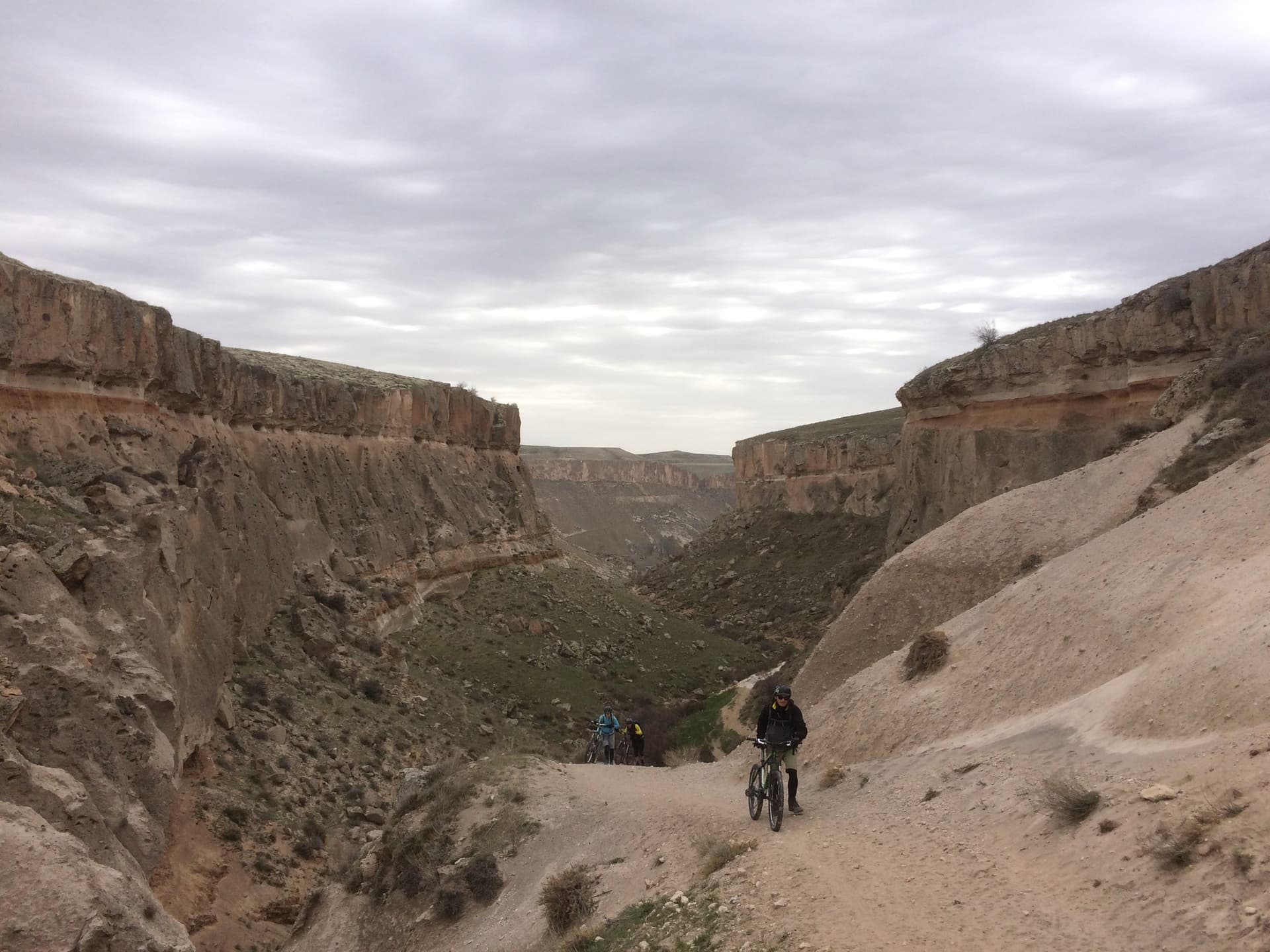 Cyclists riding a dirt track through a steep-walled canyon in Cappadocia