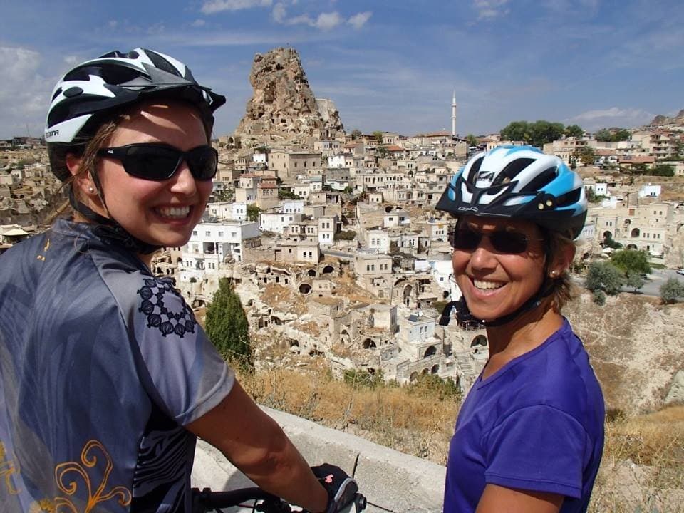 Two cyclists smiling with the hillside town of Uchisar visible behind them