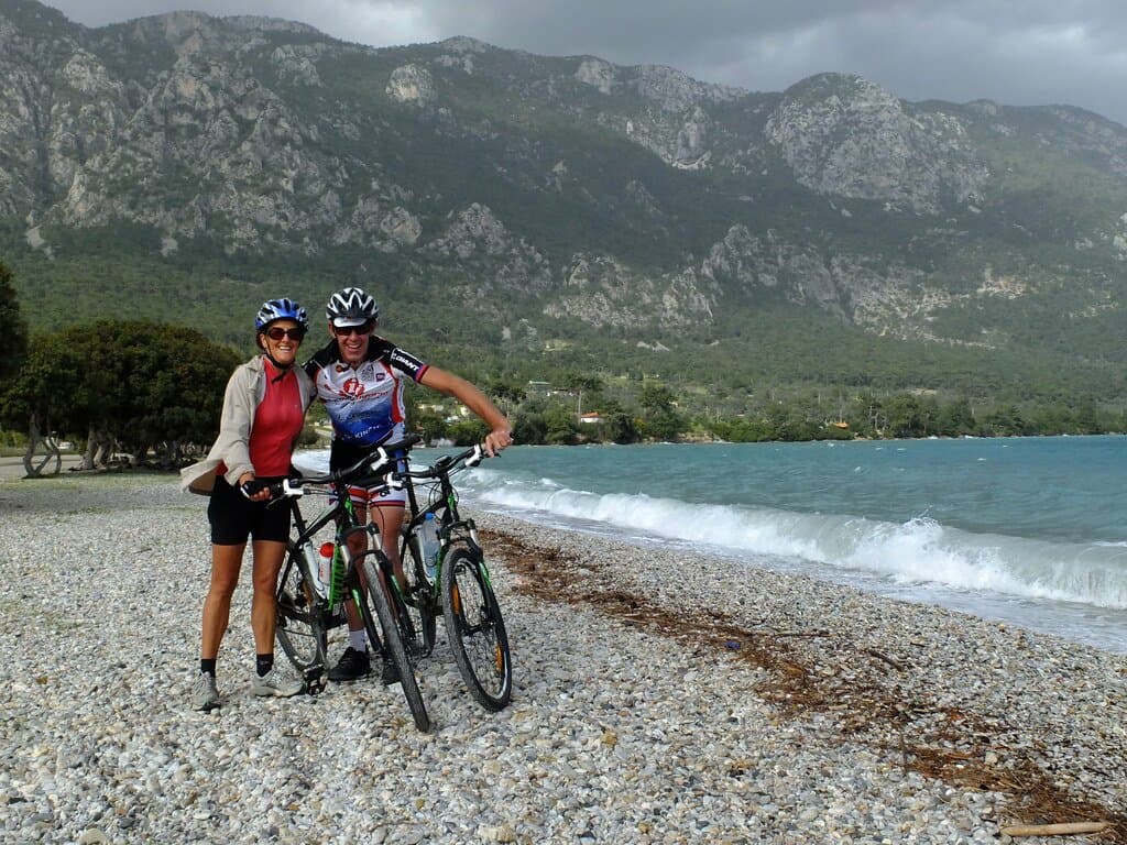 Cyclists standing with their bikes on a pebble beach on the Aegean coast