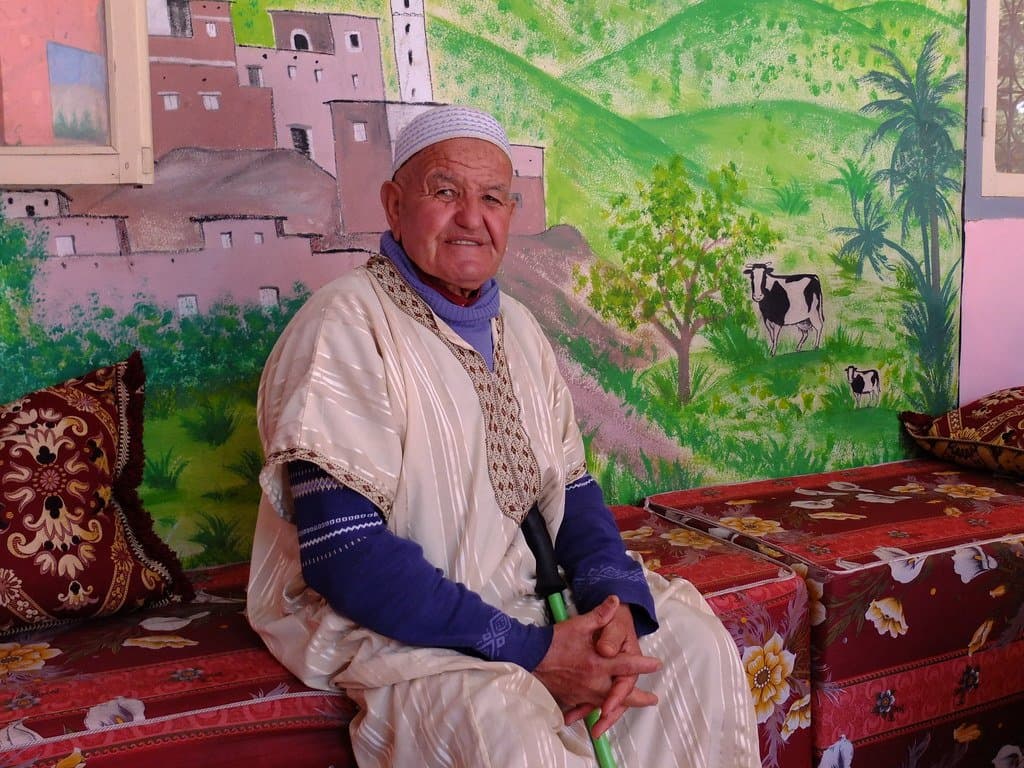 Elderly man in traditional dress sitting before a colorful mural in Morocco