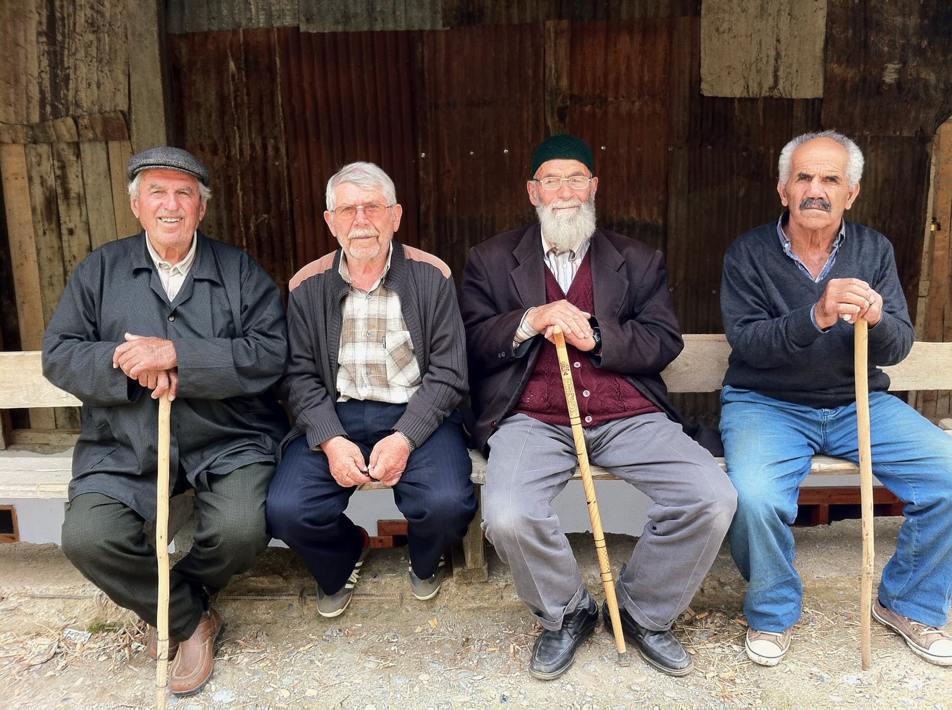 Four elderly men sitting together on a bench, each holding a wooden cane