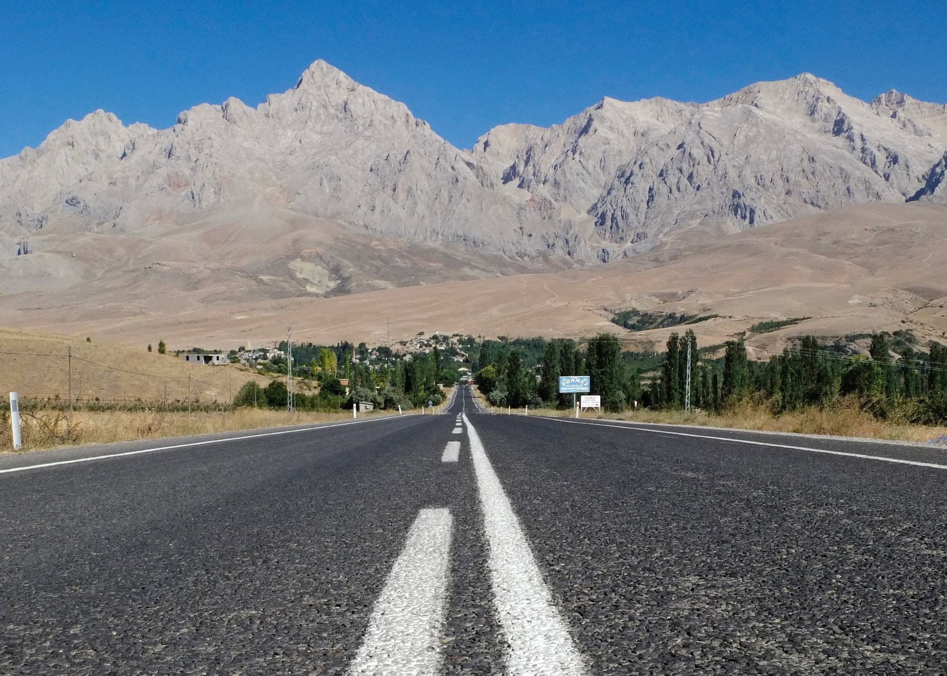 Empty paved road stretching toward a jagged mountain range ahead