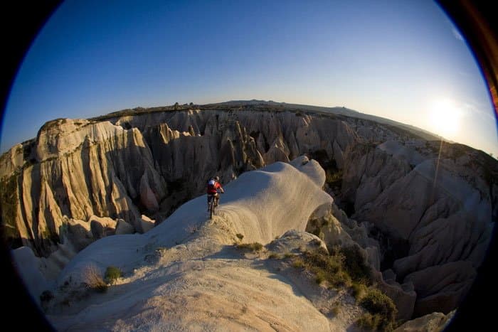 Fisheye view of a mountain biker riding a ridge of eroded rock at sunset in Cappadocia
