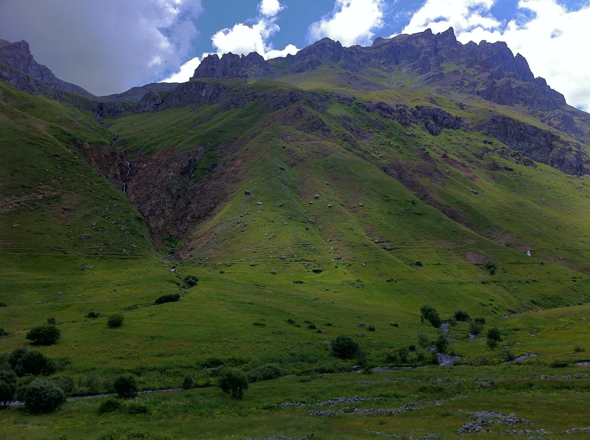 Grassy valley below a rocky peak streaked with scree in the Kackar Mountains