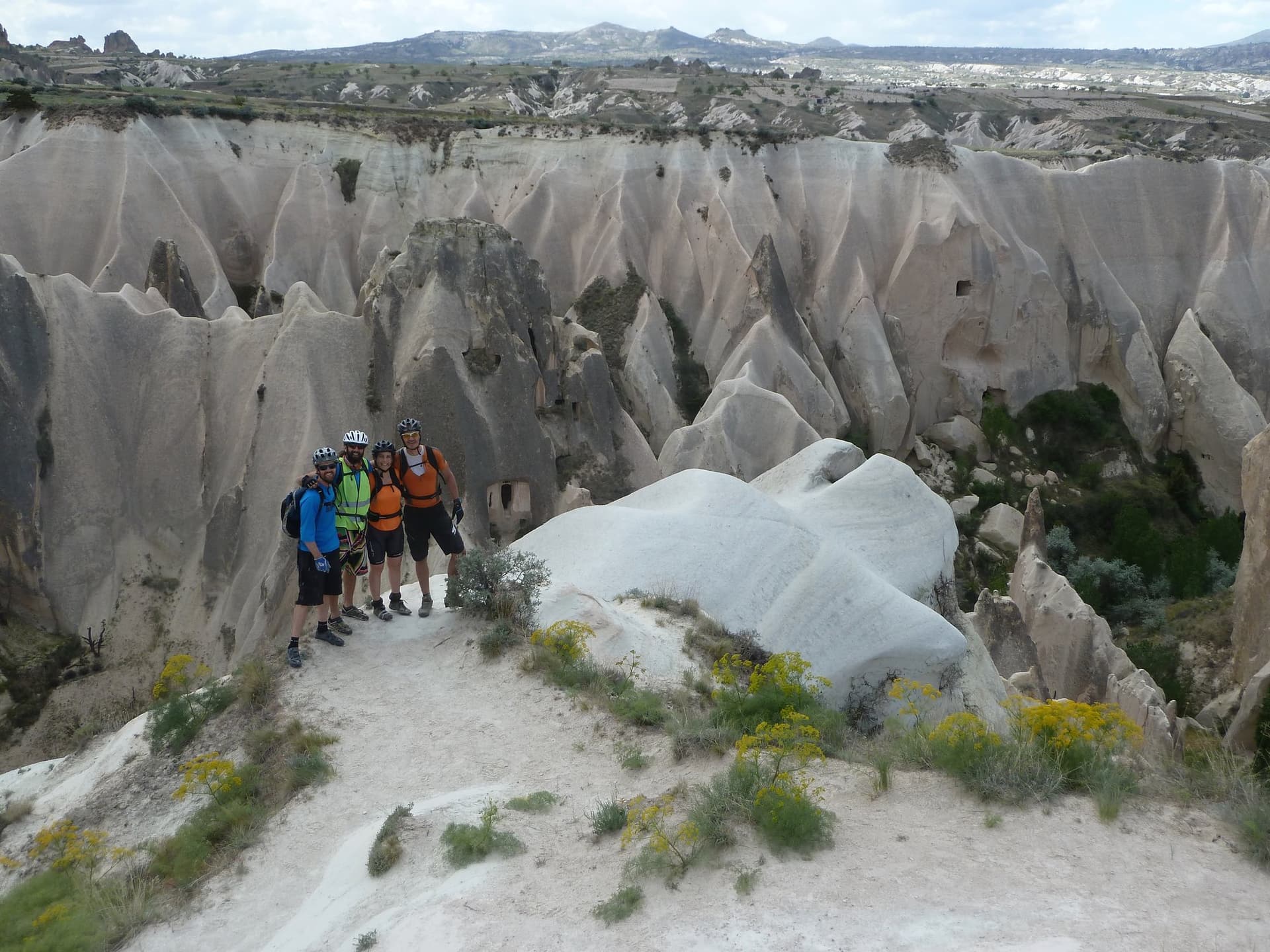 Group of mountain bikers posing among pale rock spires overlooking a Cappadocia valley