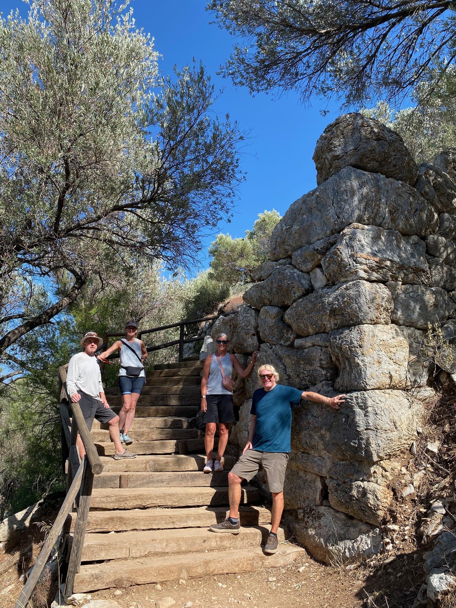 Group of walkers pausing at a stone archway and staircase among trees on the Aegean coast