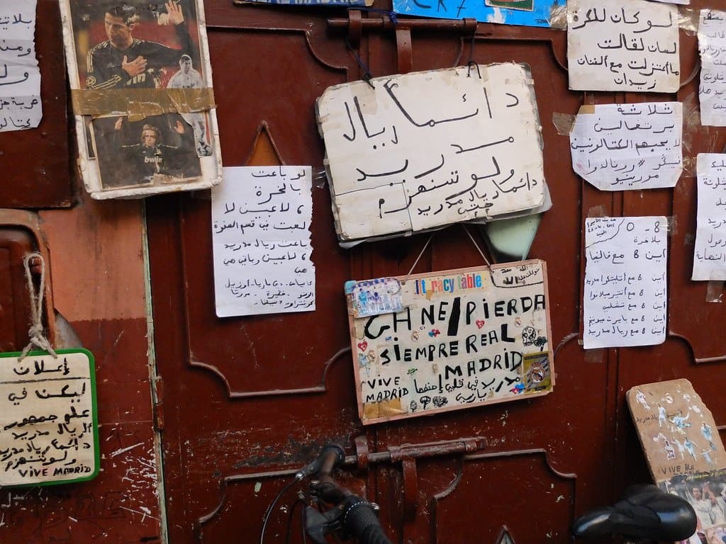 Handwritten notes and photographs pinned to a weathered red door in Morocco