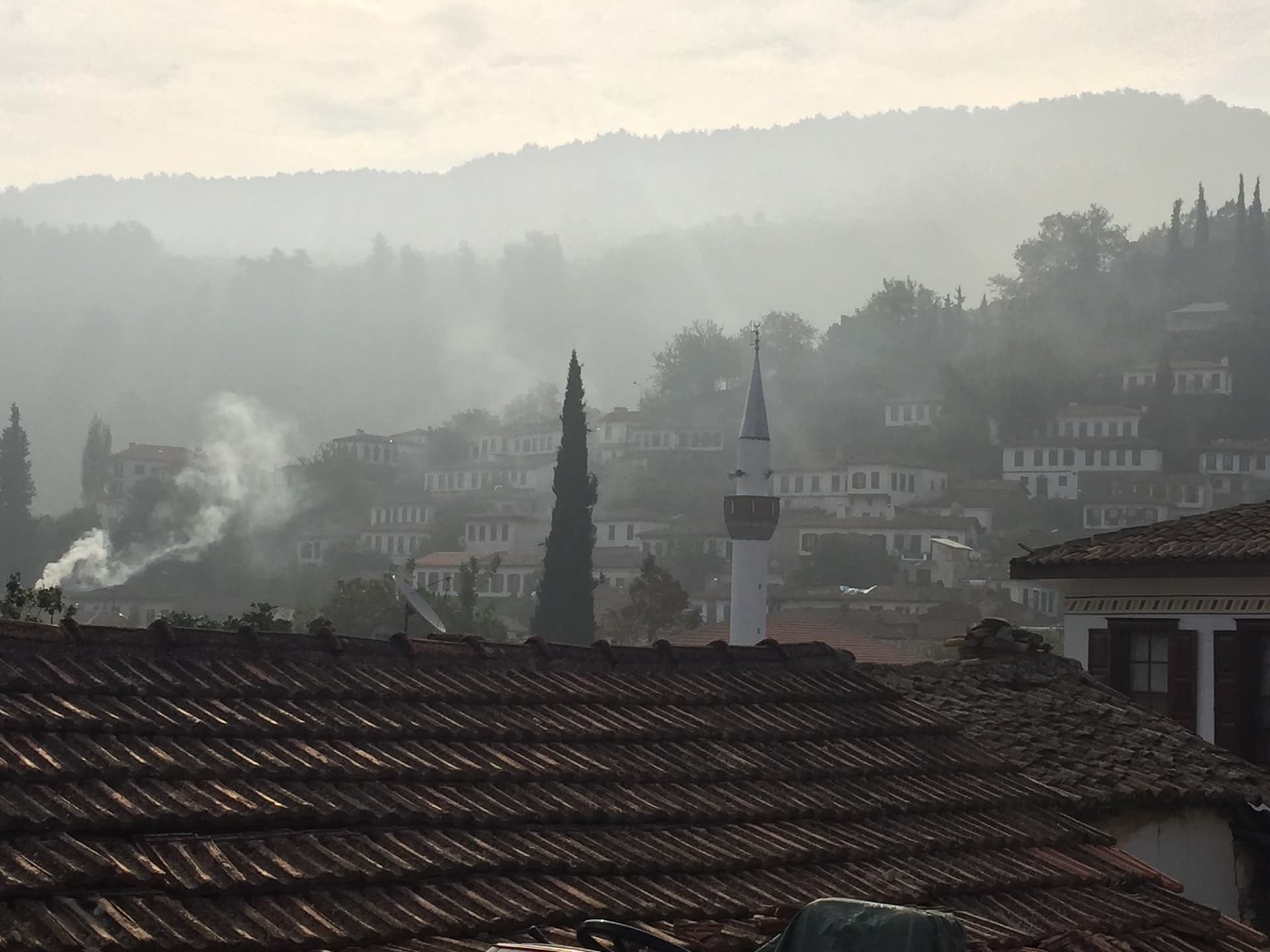 Hazy hillside village of red-tiled roofs and a minaret with rising smoke