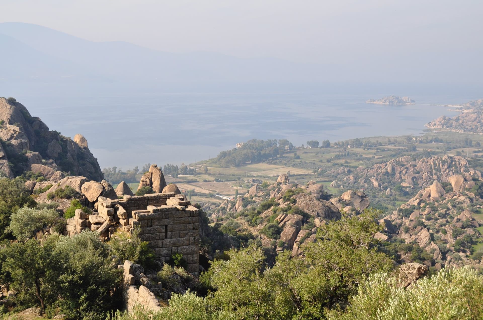 Hazy view from hilltop ruins over a lagoon and green coastal plain