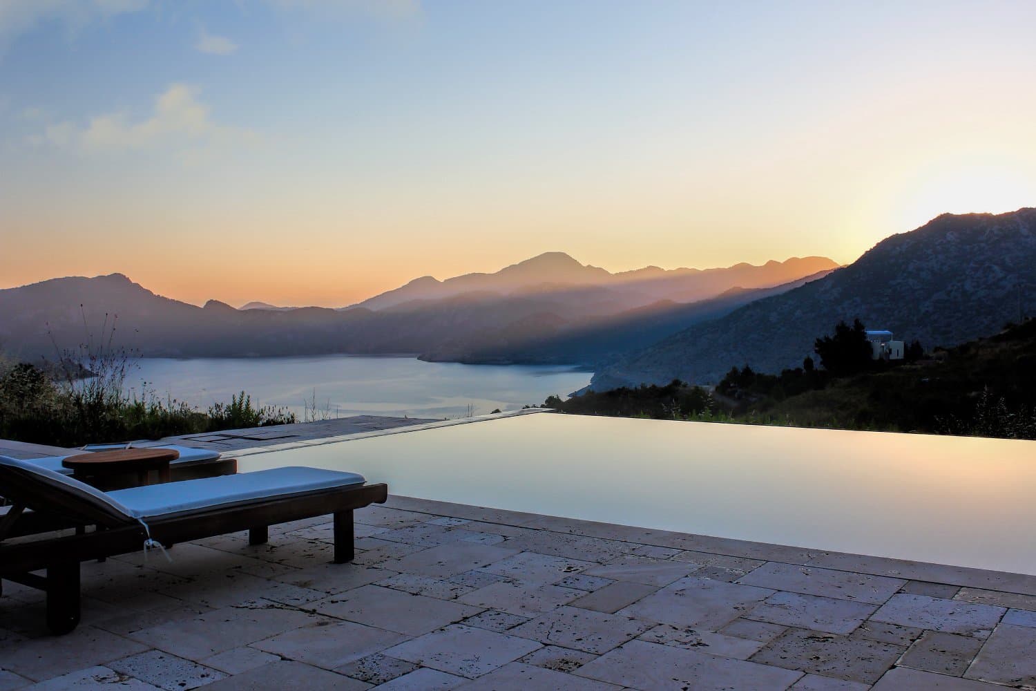 Infinity pool and sun loungers at dawn overlooking an Aegean bay from a boutique hotel terrace
