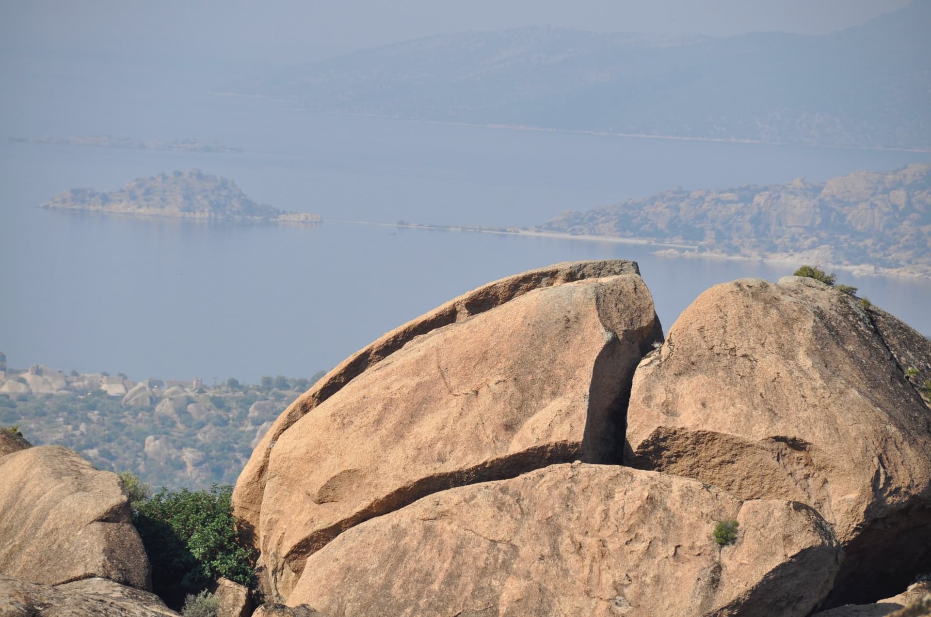 Large boulders on a rocky hilltop overlooking a hazy coastal lagoon