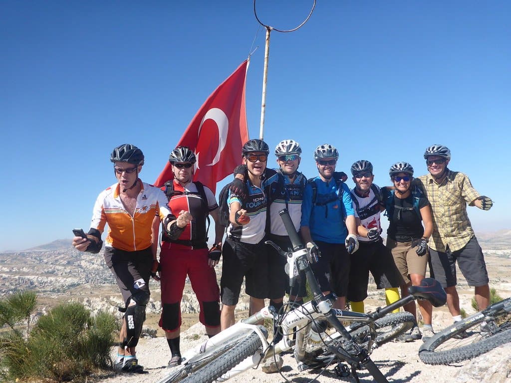 Large group of cyclists posing with a Turkish flag on a hilltop