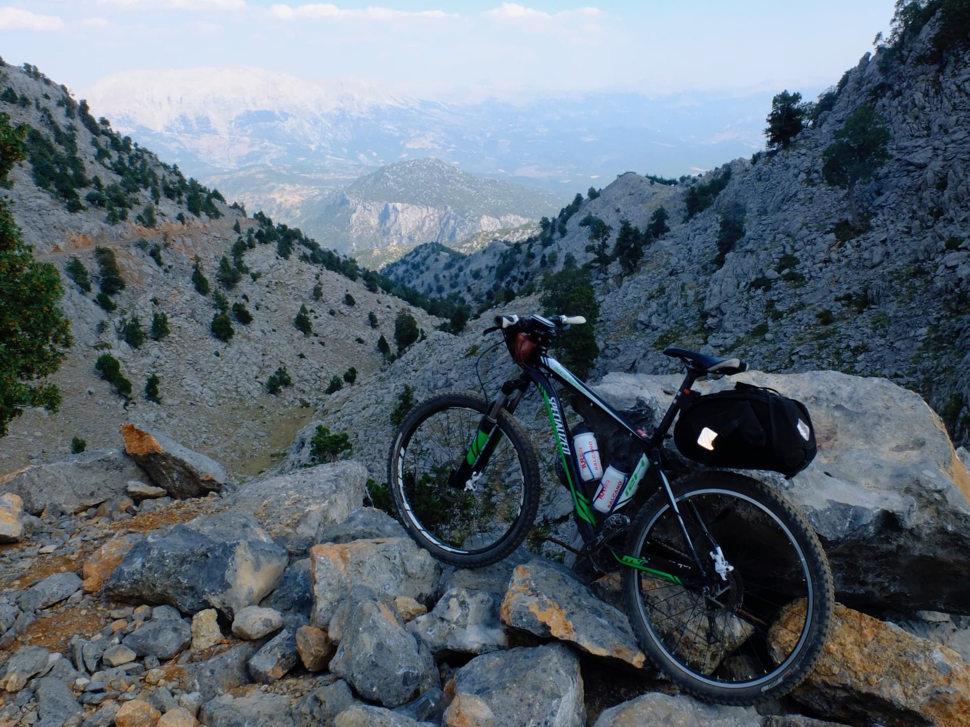 Loaded mountain bike resting on rocks with snow-capped Taurus Mountains peaks beyond