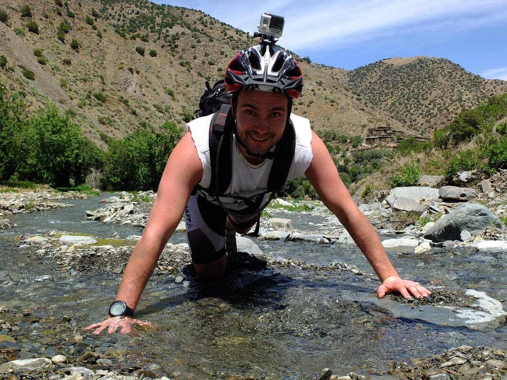 Man crossing a shallow river on hands and knees in the Atlas Mountains, Morocco