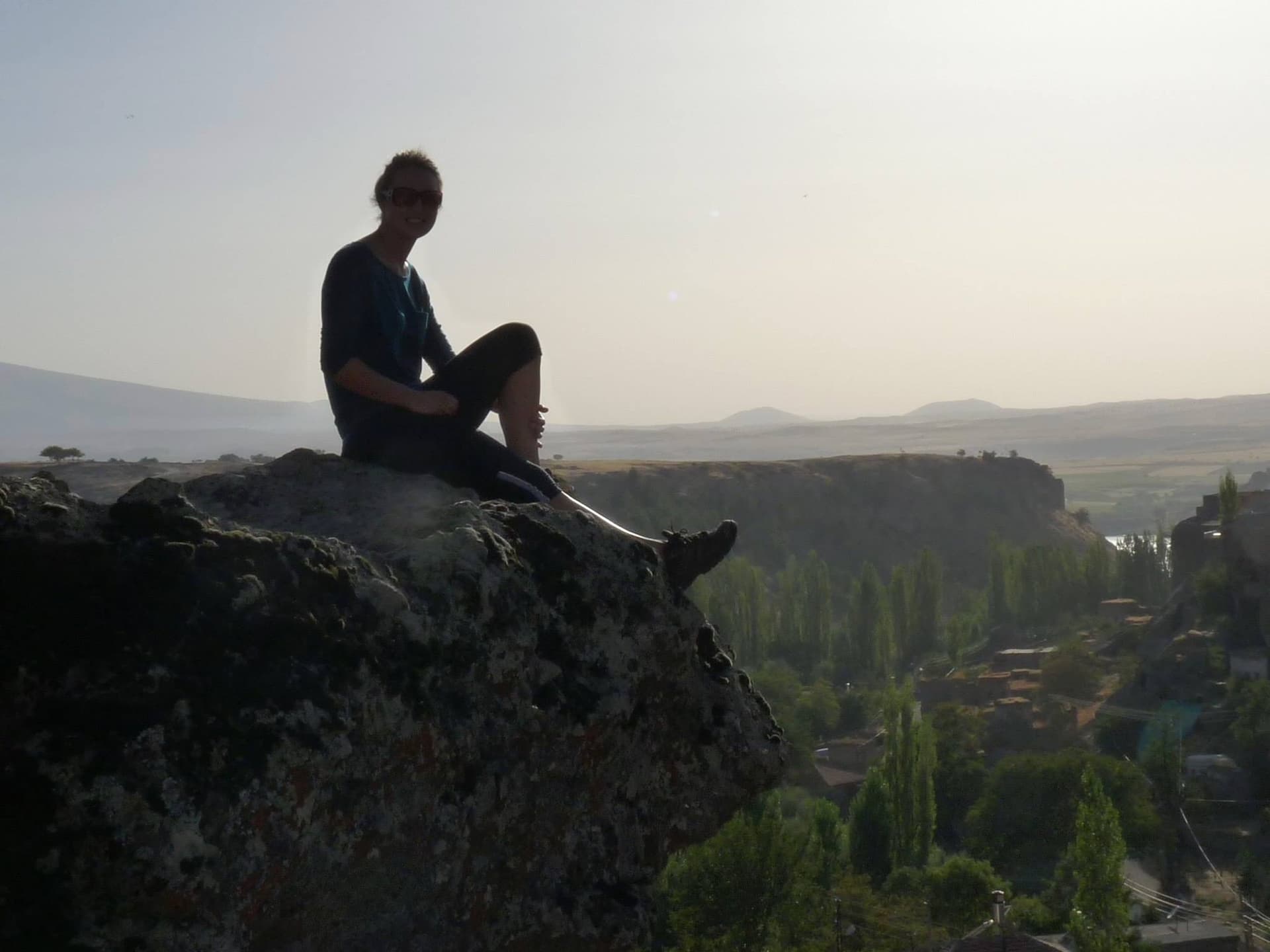 Man sitting on a rocky cliff edge overlooking a green valley village