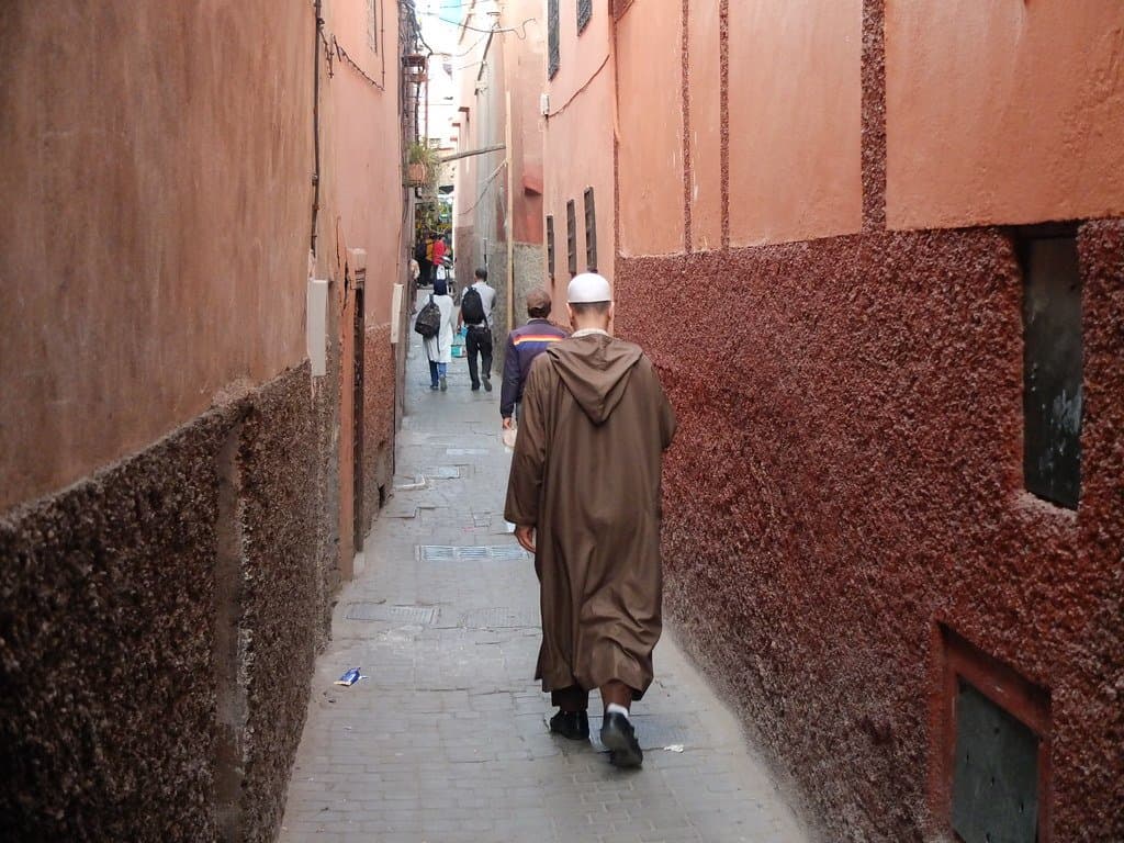 Man in traditional robe walking through a narrow red-walled alley in Morocco