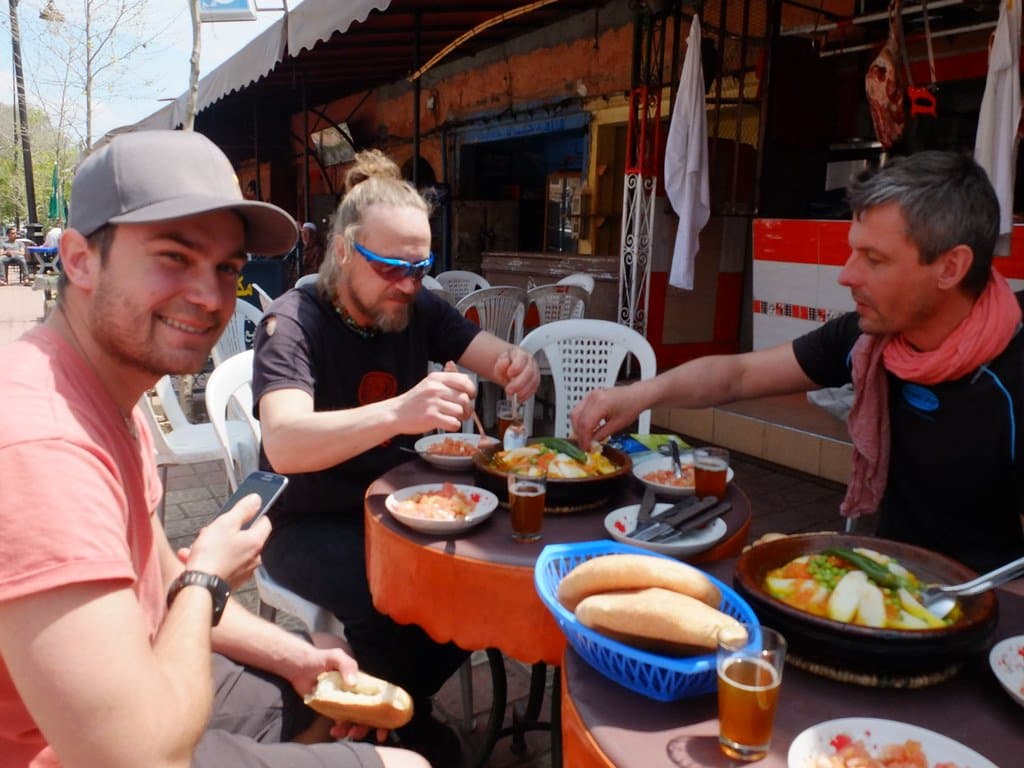 Men sharing a tagine meal at an outdoor table in a Moroccan town