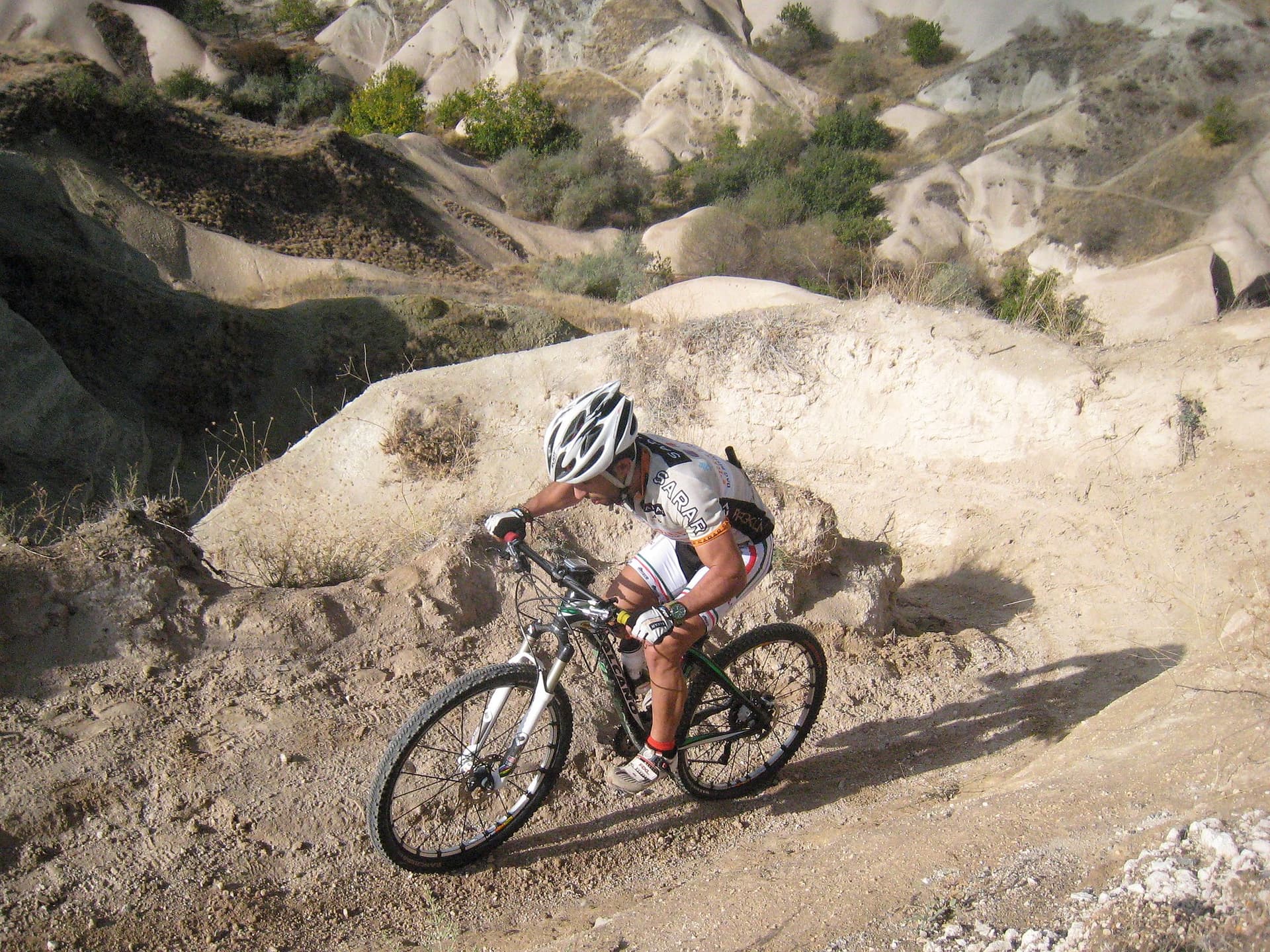 Mountain biker descending a sandy trail between pale rock formations in Cappadocia