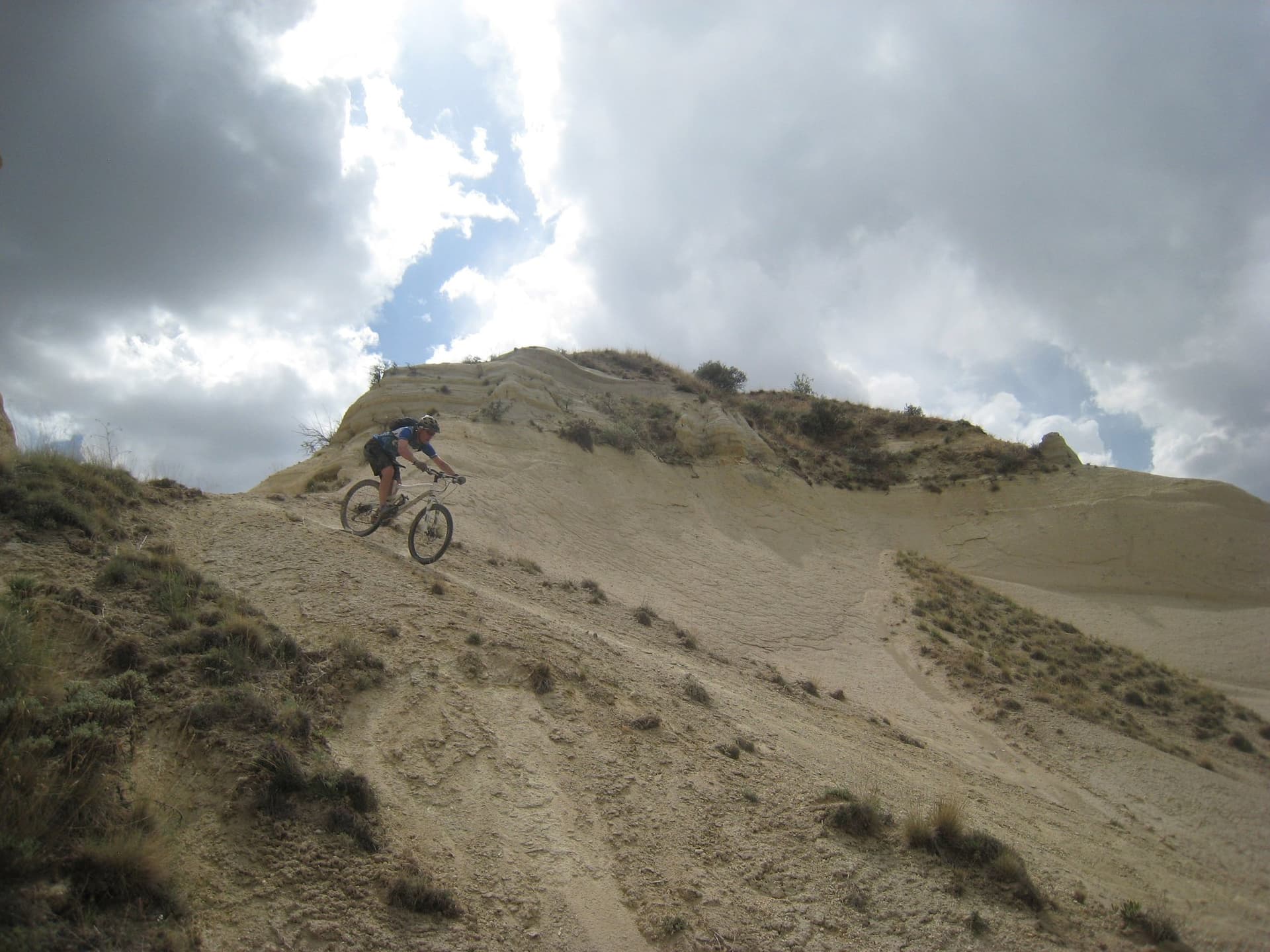 Mountain biker descending a steep dirt dune under a cloudy sky in Cappadocia