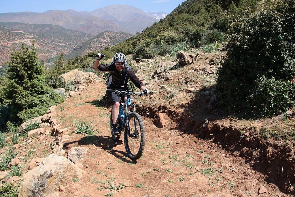 Mountain biker riding a dirt trail across a red hillside in the Atlas Mountains, Morocco