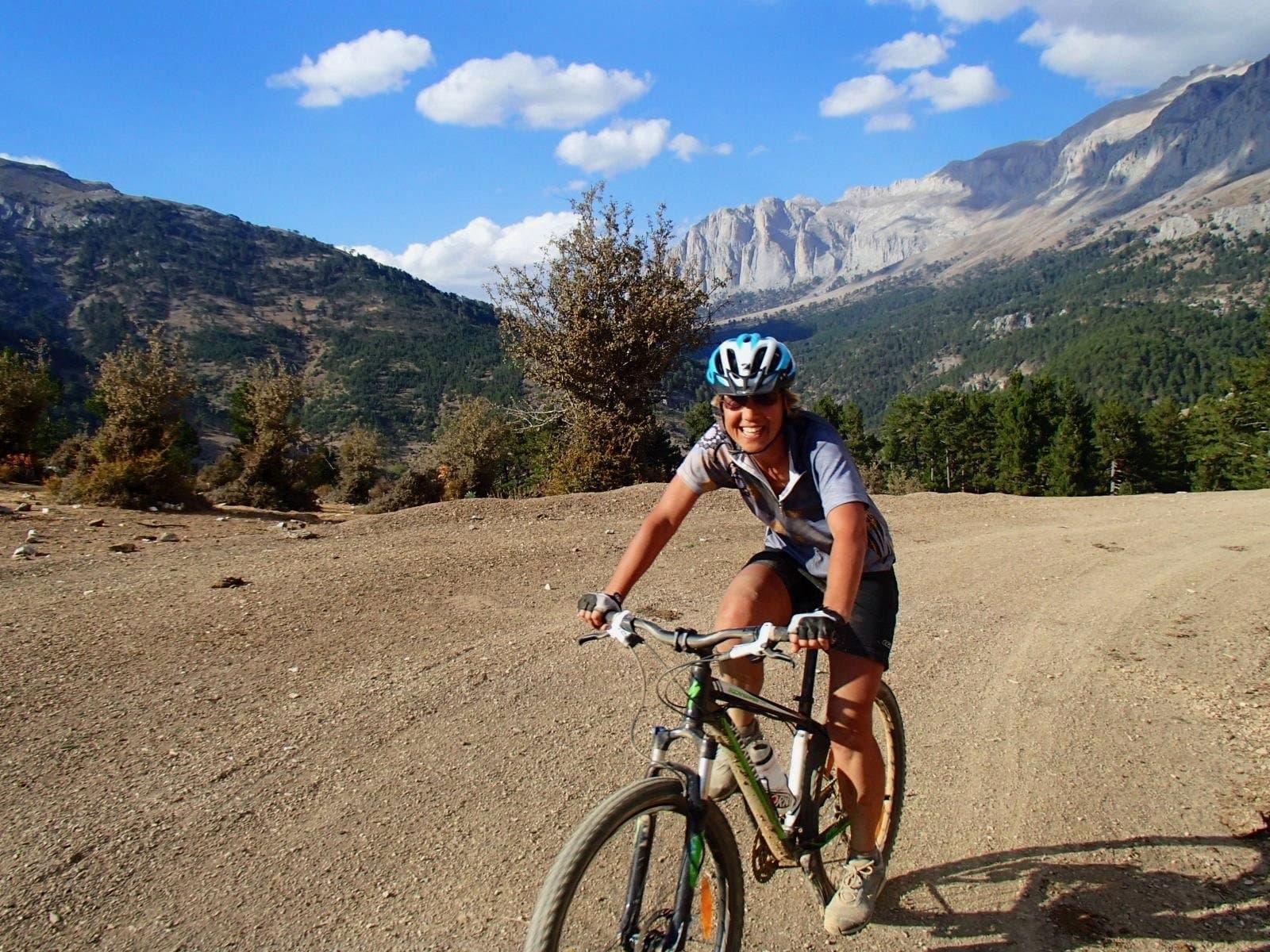 Mountain biker riding a dirt trail with snow-streaked Taurus Mountains peaks behind