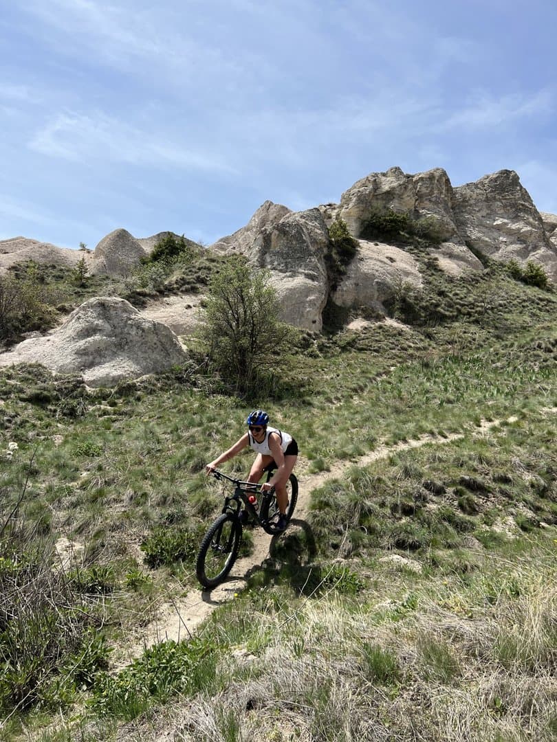 Mountain biker riding a grassy singletrack trail below jagged rock formations
