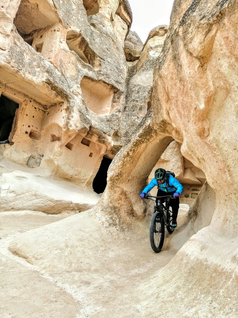Mountain biker riding through a narrow rock-carved passage between cave dwellings