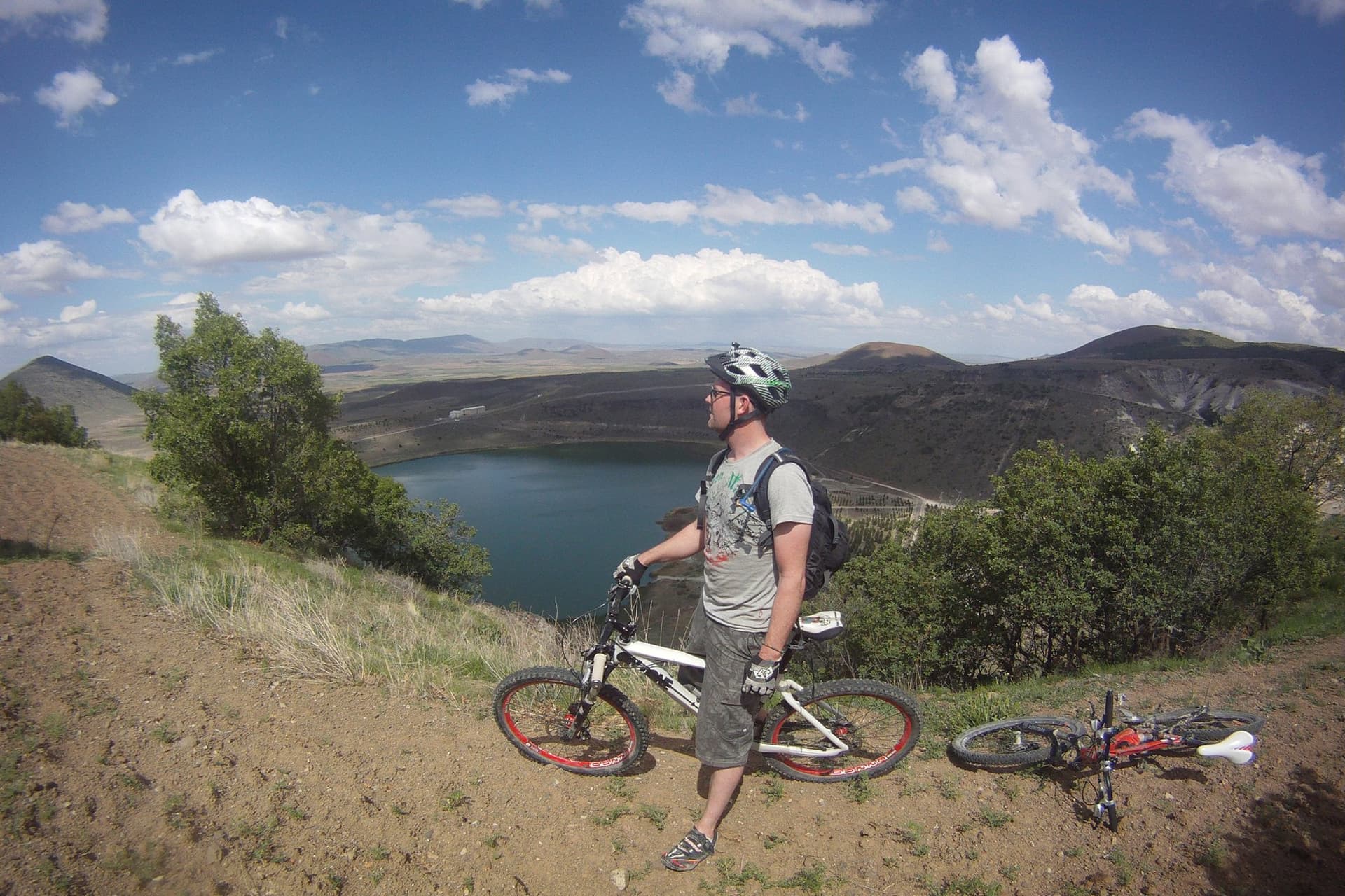 Mountain biker standing beside two bikes overlooking a lake in the Cappadocia countryside