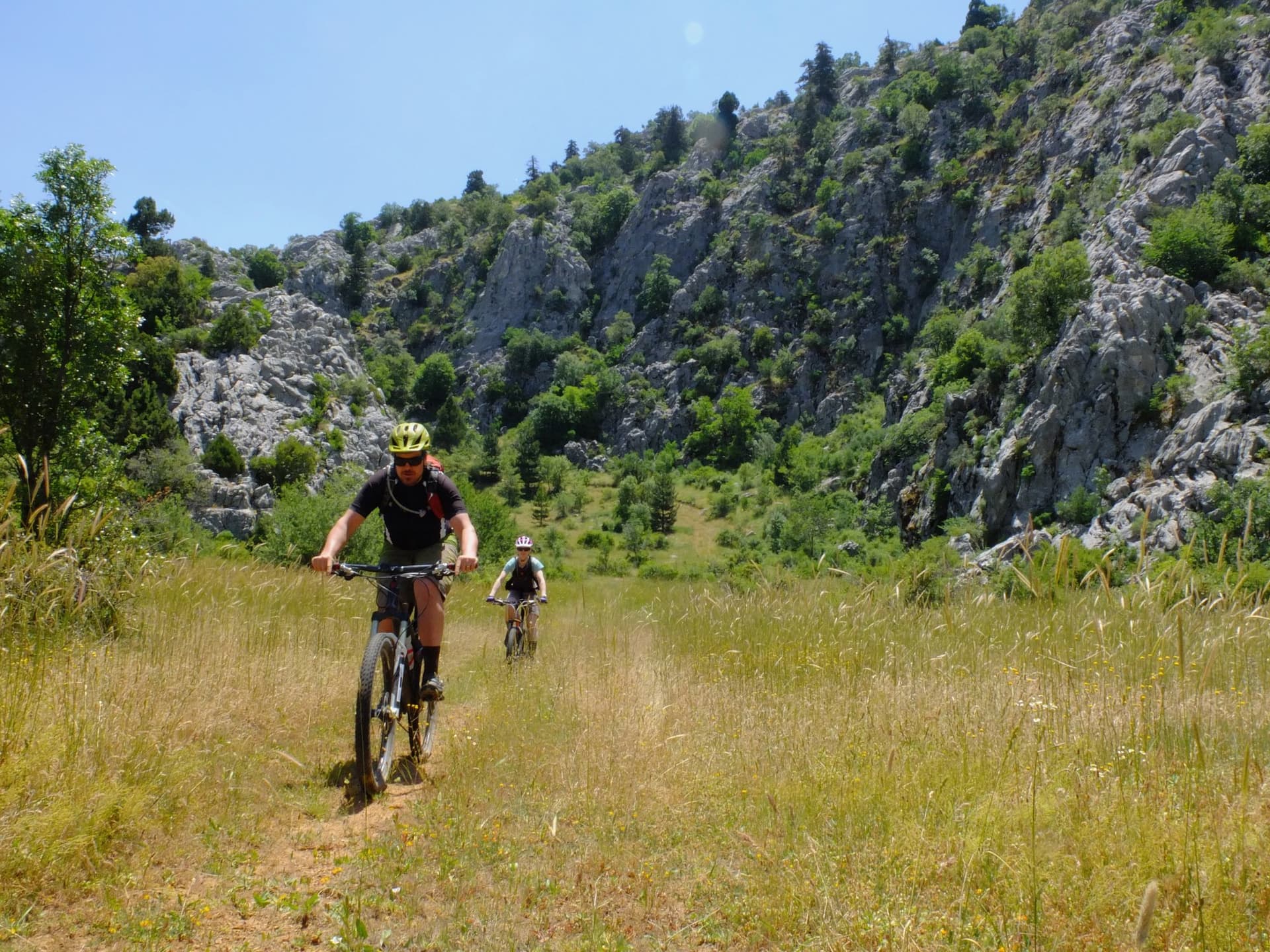 Mountain bikers crossing a grassy meadow below a rocky ridge in the Taurus Mountains