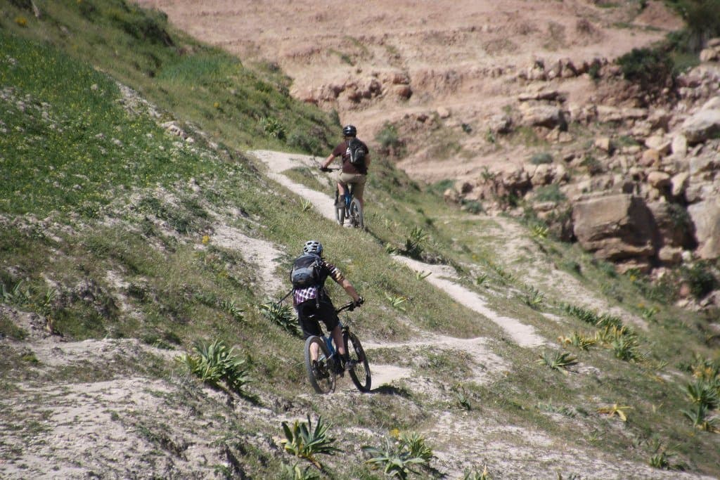 Mountain bikers riding down a dirt track through a green valley in Morocco